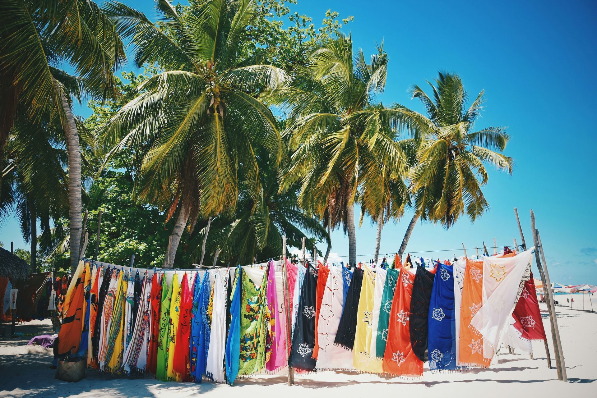 Beach scene with colorful sarongs hanging on a rack, palm trees on Nosy Iranj, Madagascar.
