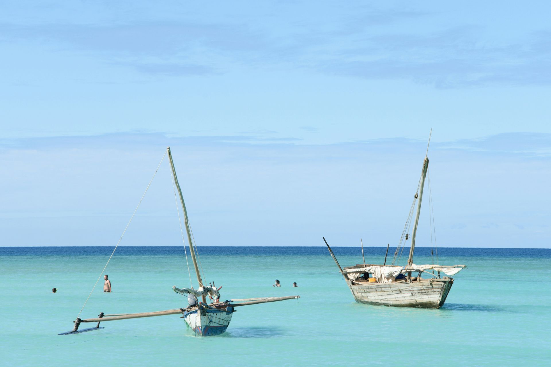 Two weathered boats float in turquoise water; swimmers in background on Nosy Iranj, Madagascar.
