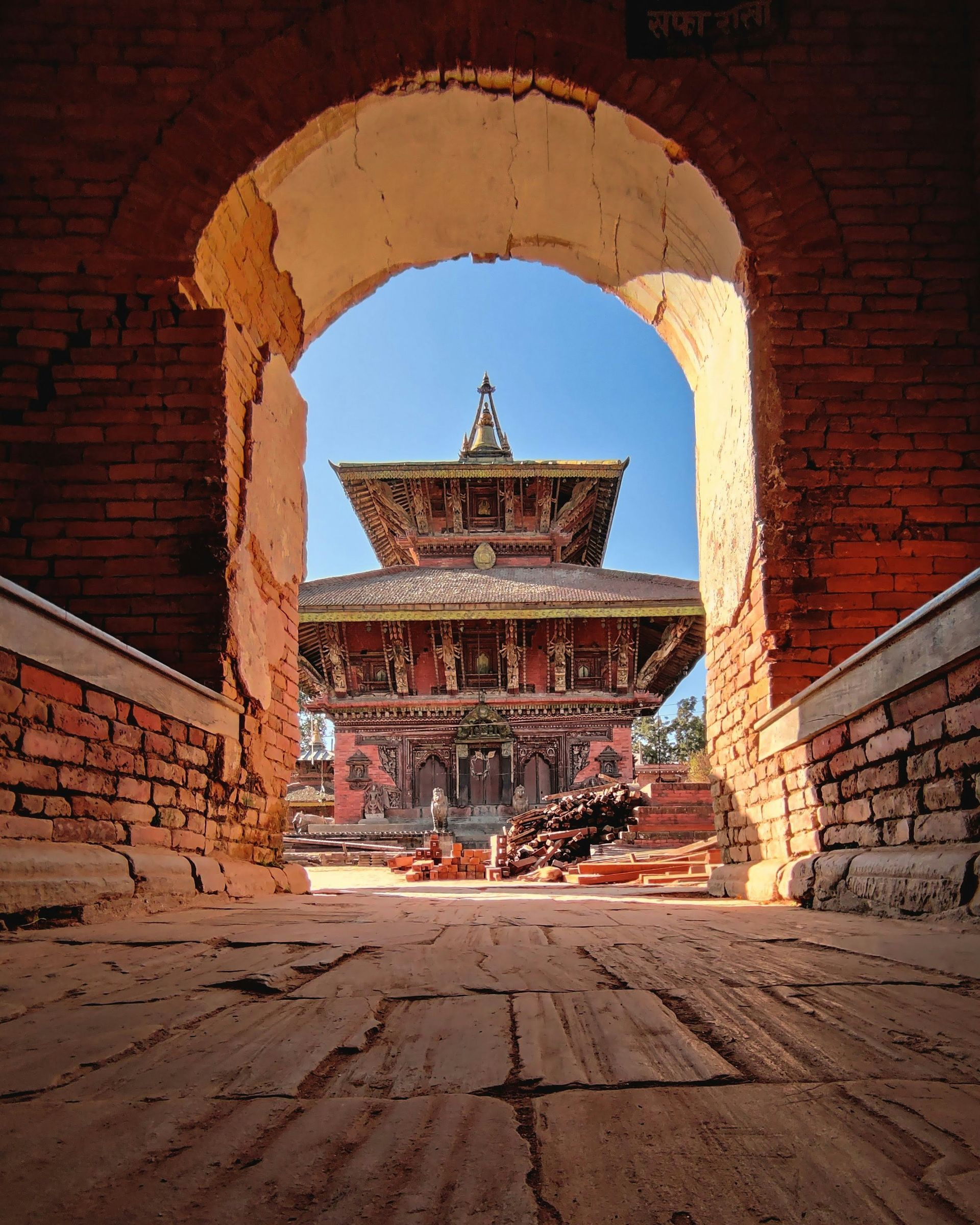A brick archway frames a detailed Nepalese temple in Kathmandu, Nepal.