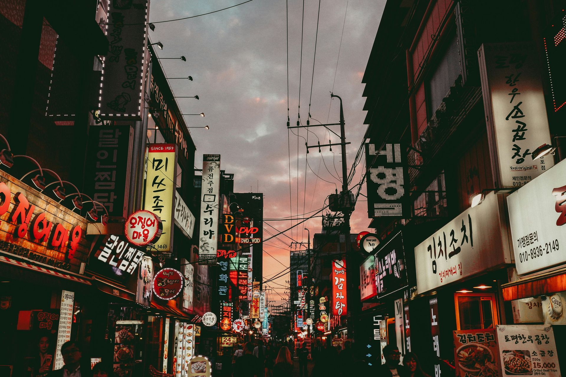 A bustling street in Seoul, lined with lit-up signs, under an evening sky in South Korea.