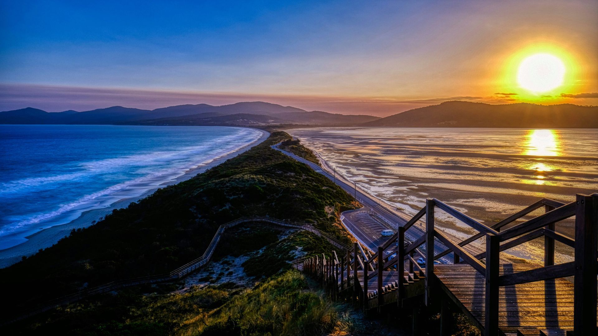 A sunset over a beach with stairs leading up to it in Tasmania, Australia.