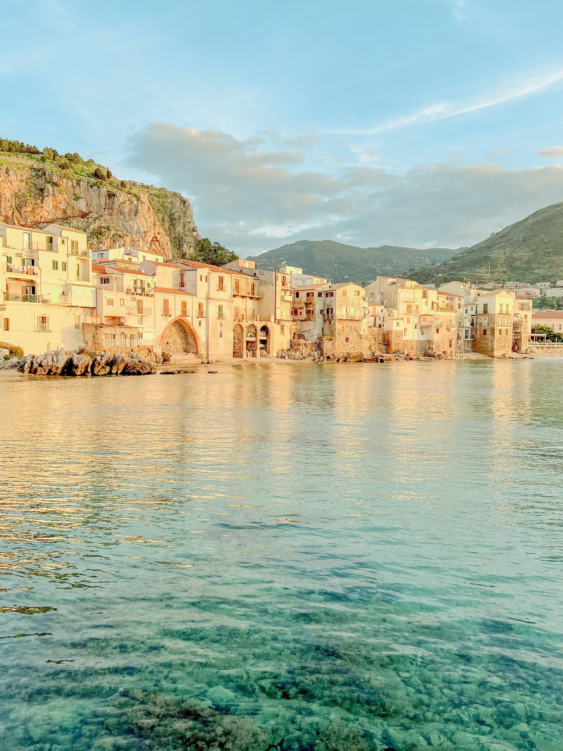 A small town in the middle of a body of water with mountains in the background in Sicily.