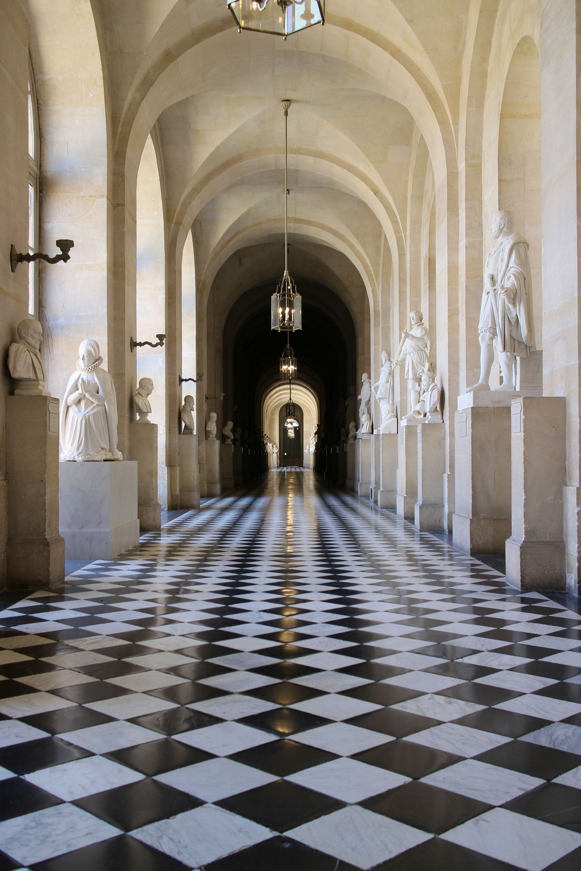A long hallway with a checkered floor and statues at the Palace of Versailles in France.