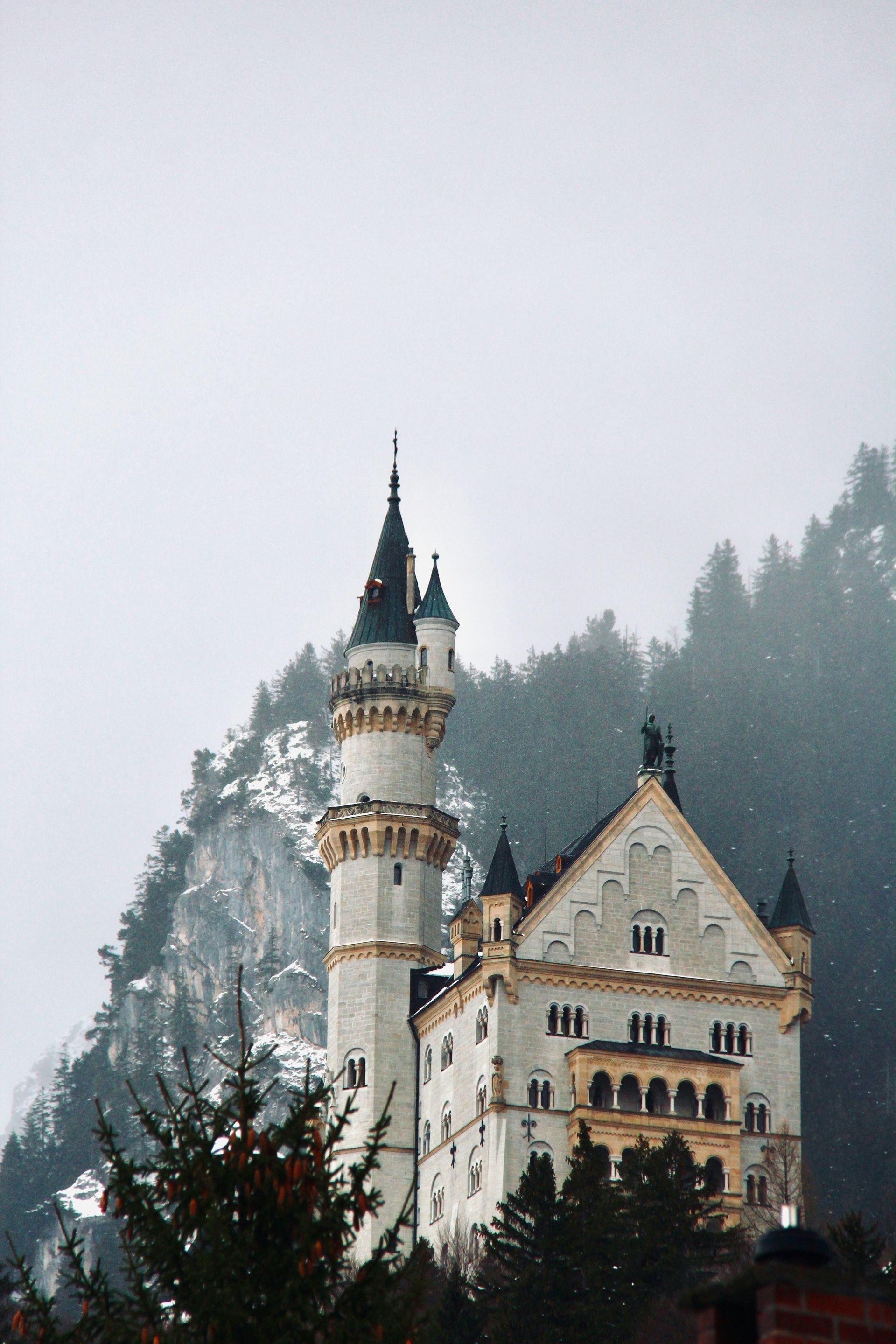 Neuschwanstein Castle in winter, tall white tower, snow-covered mountain backdrop.