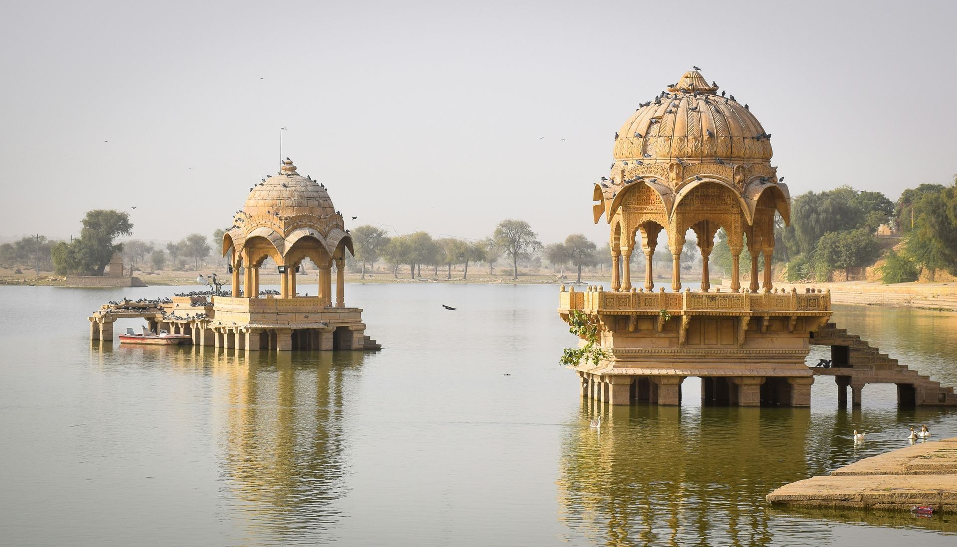 Two ornate, golden-toned sandstone pavilions on a lake in Jaisalmer, India.