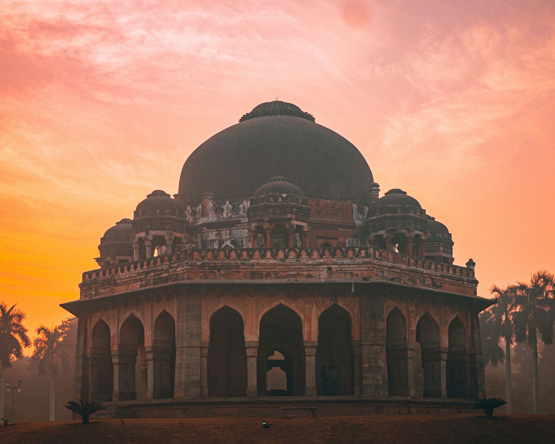 Dome-shaped tomb against an orange and pink sunset; arches along the base in New Delhi, India.