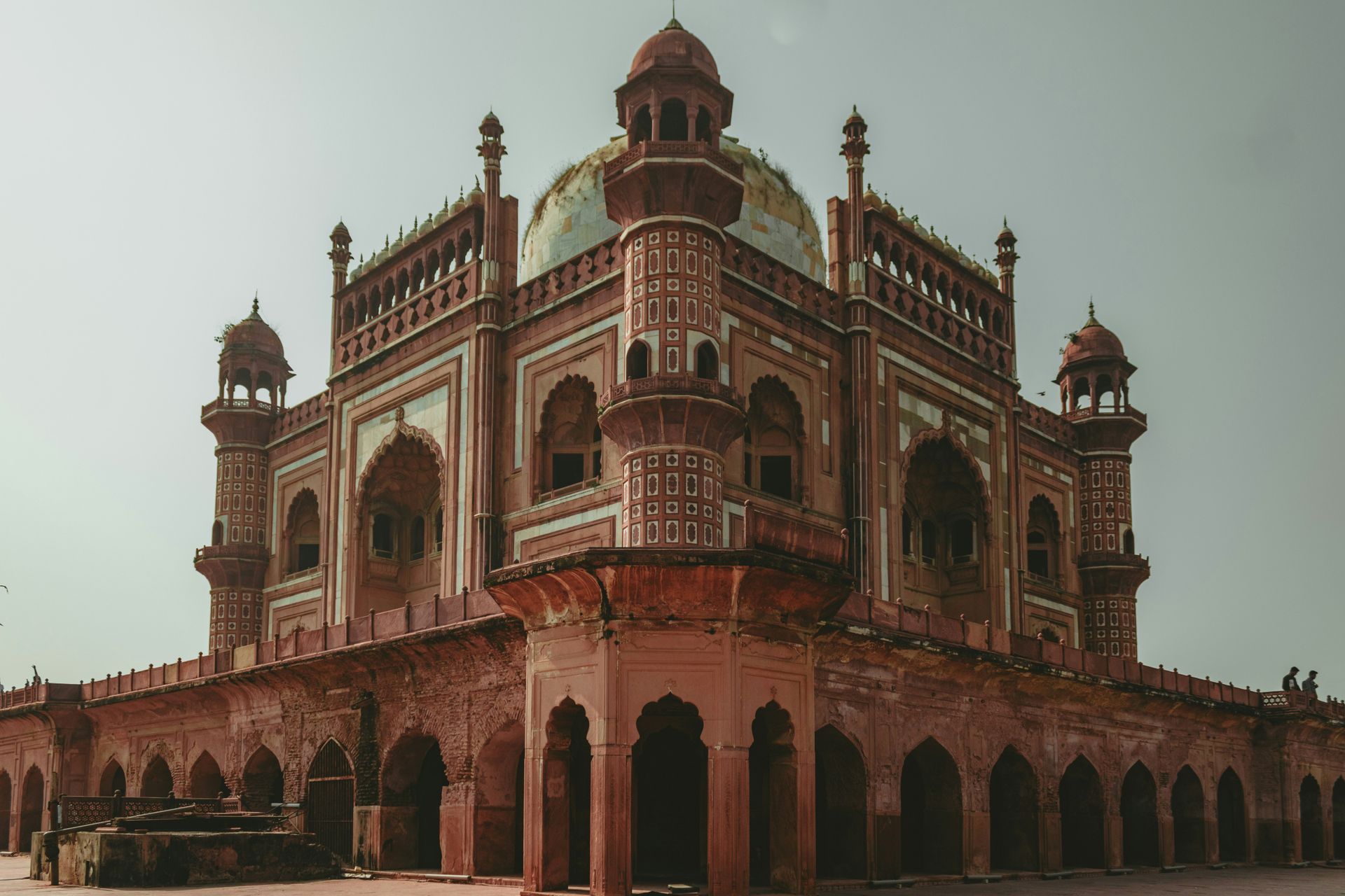 Red brick tomb with arched windows and a dome against a pale sky in New Delhi, India.