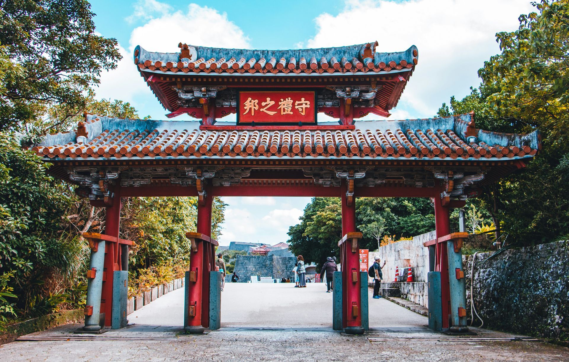 Ornate red and gray gate with a sign in Japanese, leading into a stone pathway