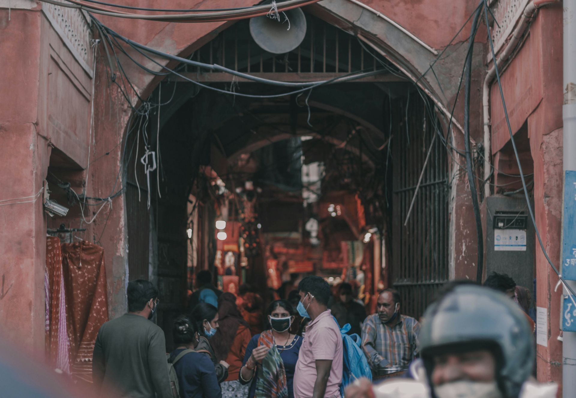 Entrance archway with people; red walls, wires, and a blurry interior in Jaipur, India.