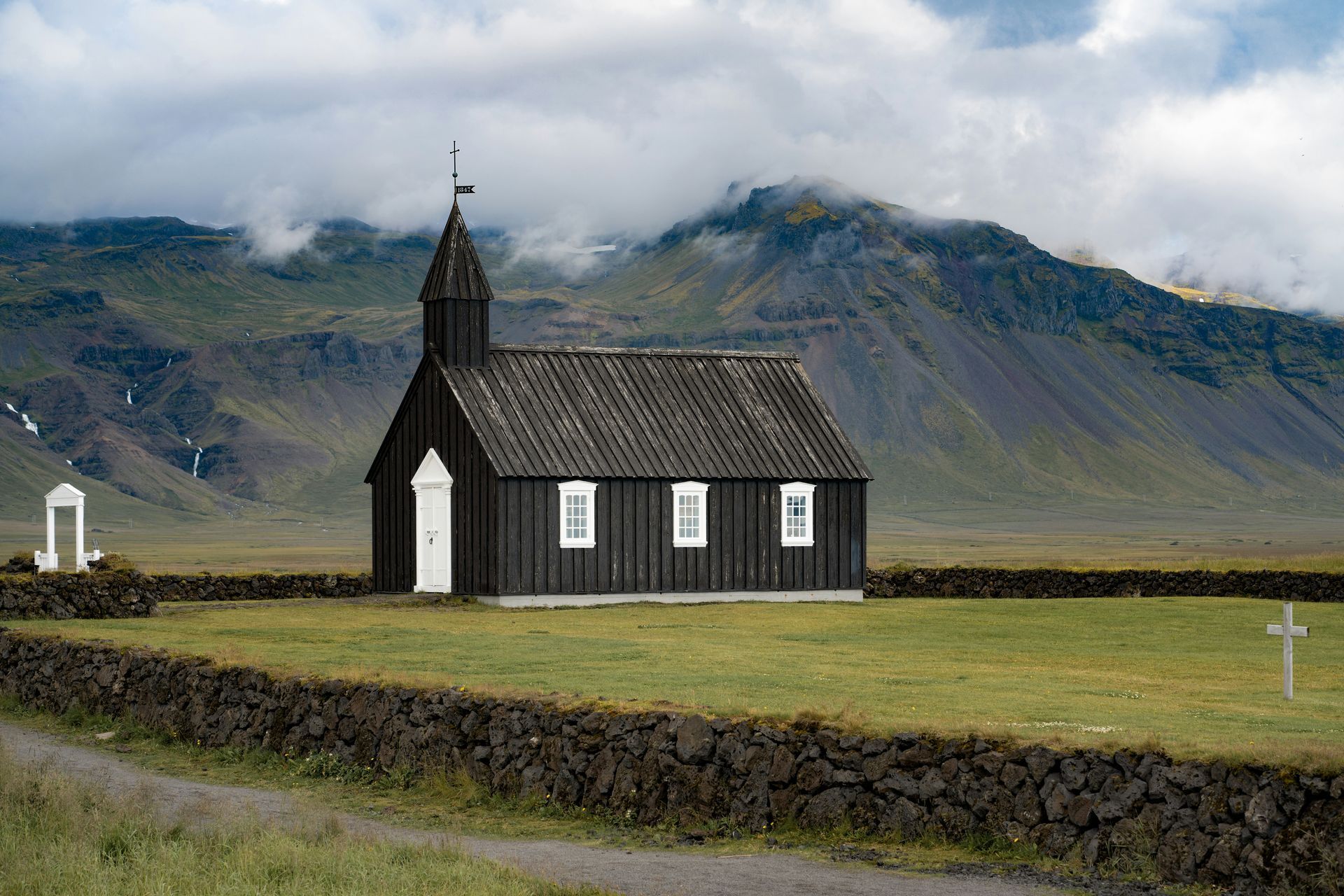 Black church with white trim in a grassy field, with mountains in the background in Snæfellsnes, Iceland.