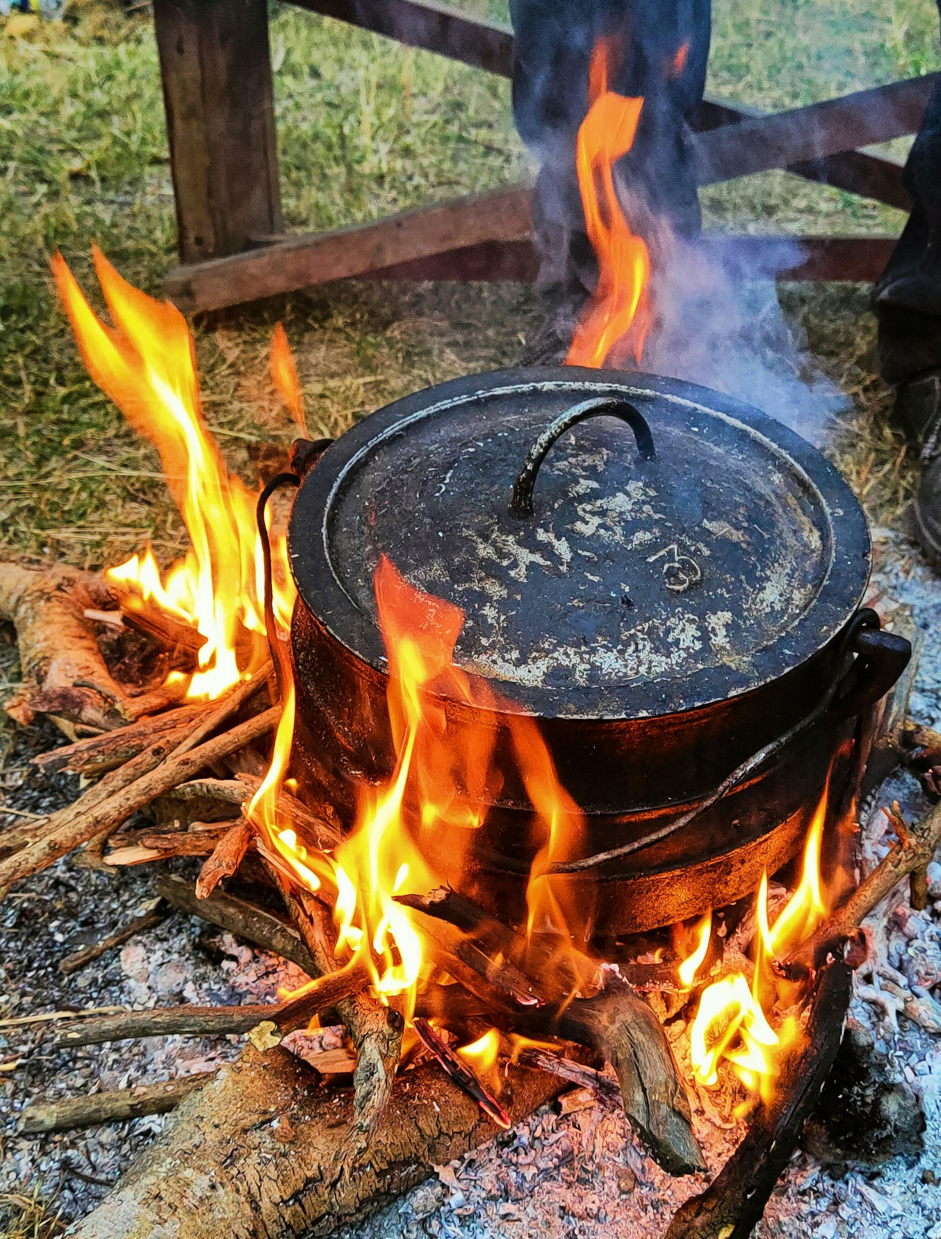 A cast iron pot with lid sits over a roaring outdoor fire, making traditional Potjiekos in South Africa.