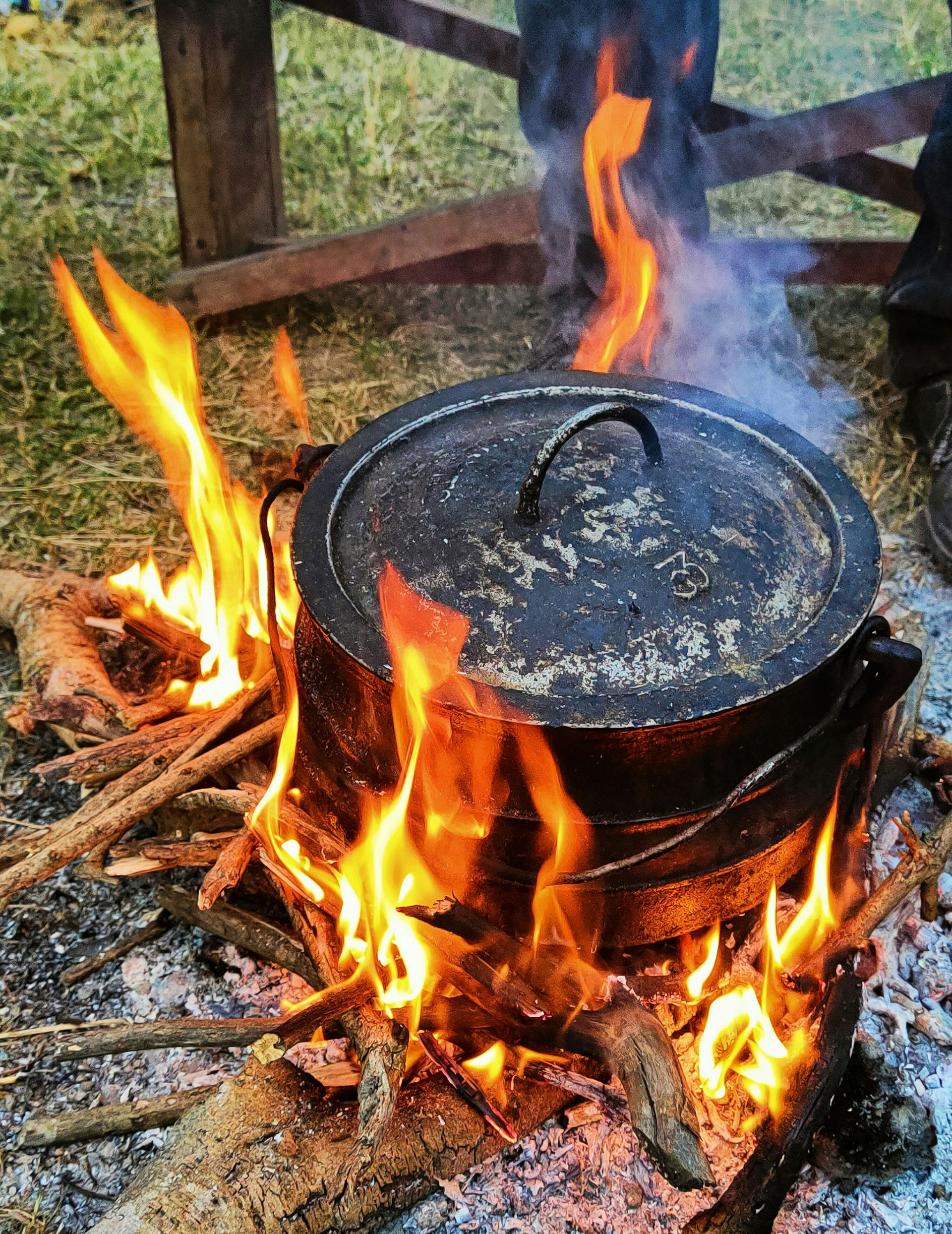 A cast iron pot with lid sits over a roaring outdoor fire, making traditional Potjiekos in South Africa.