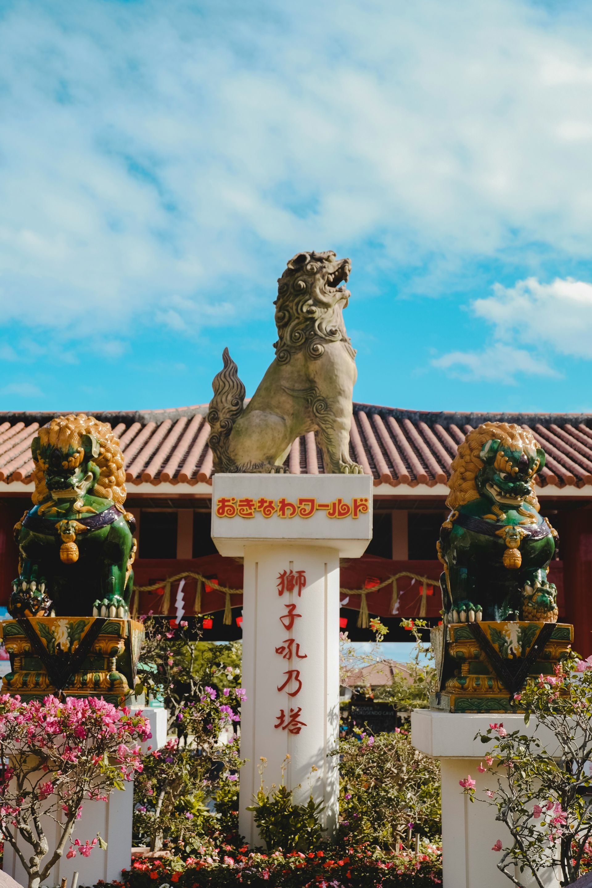 Stone guardian lions in front of a red-roofed building in Okinawa, Japan.