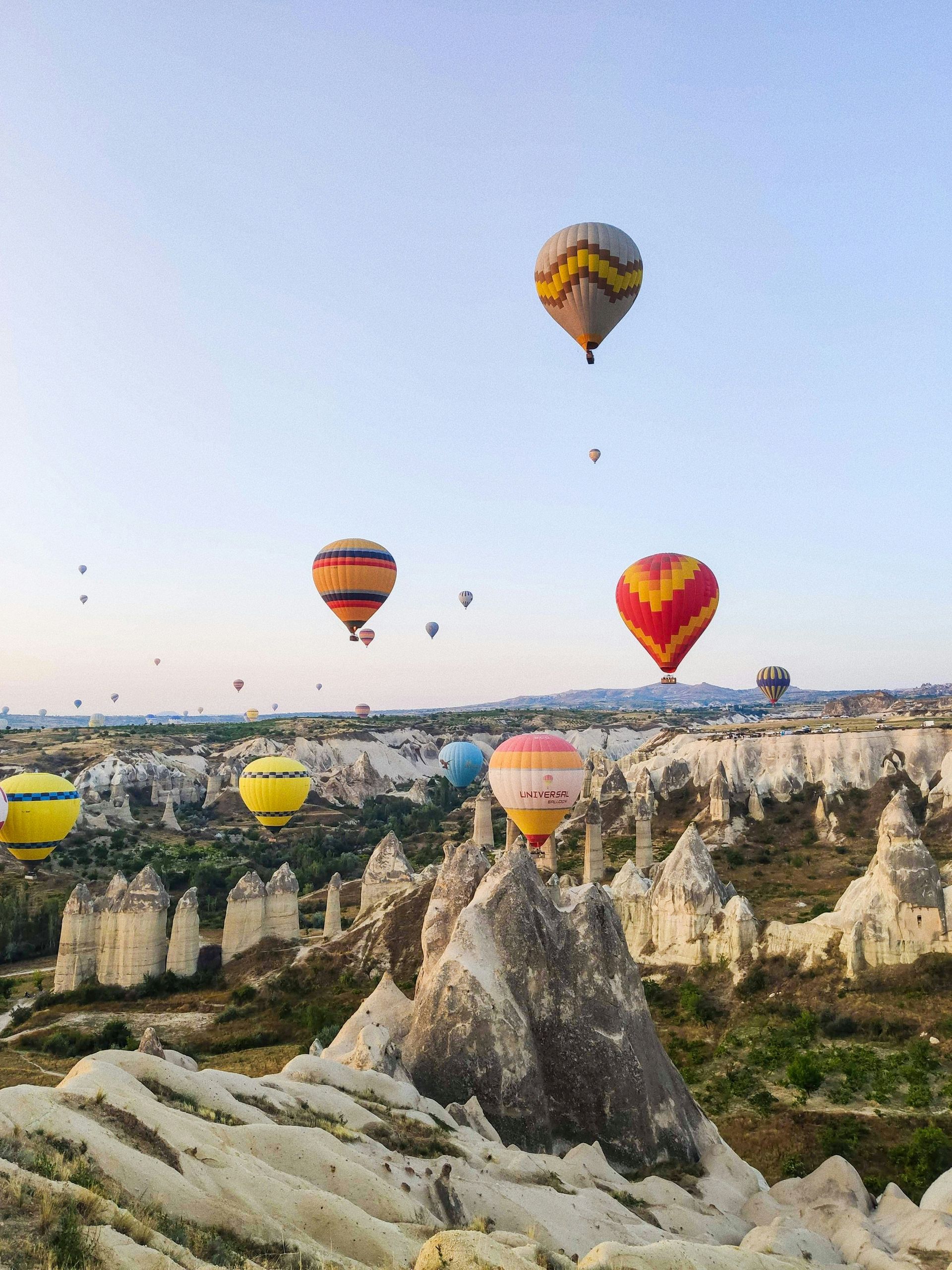 Hot air balloons over Cappadocia's rock formations, blue sky.