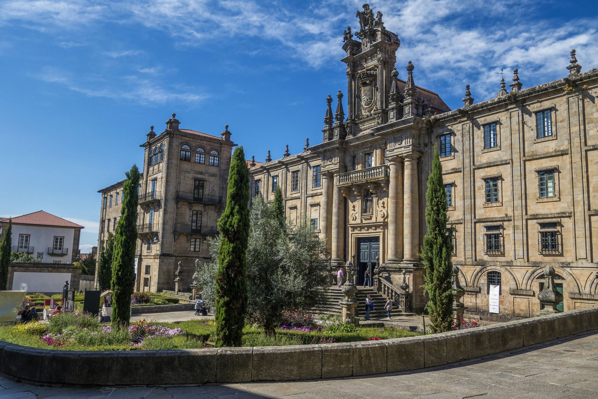 Large stone building with ornate facade, trees, and flower beds in Santiago de Compostela, Spain.