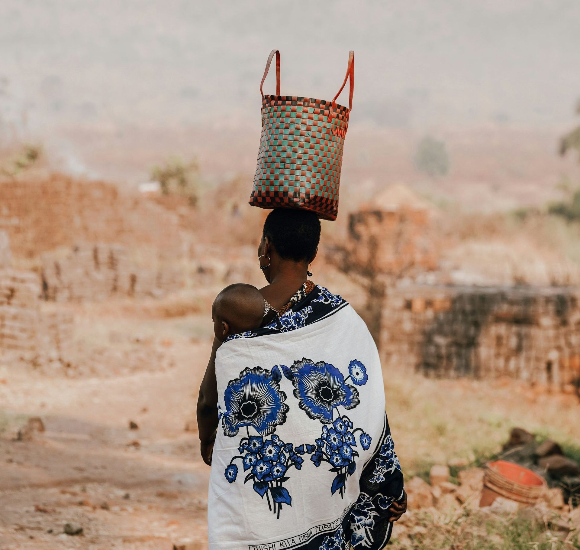 A woman is carrying a baby and a basket on her head in Tanzania.