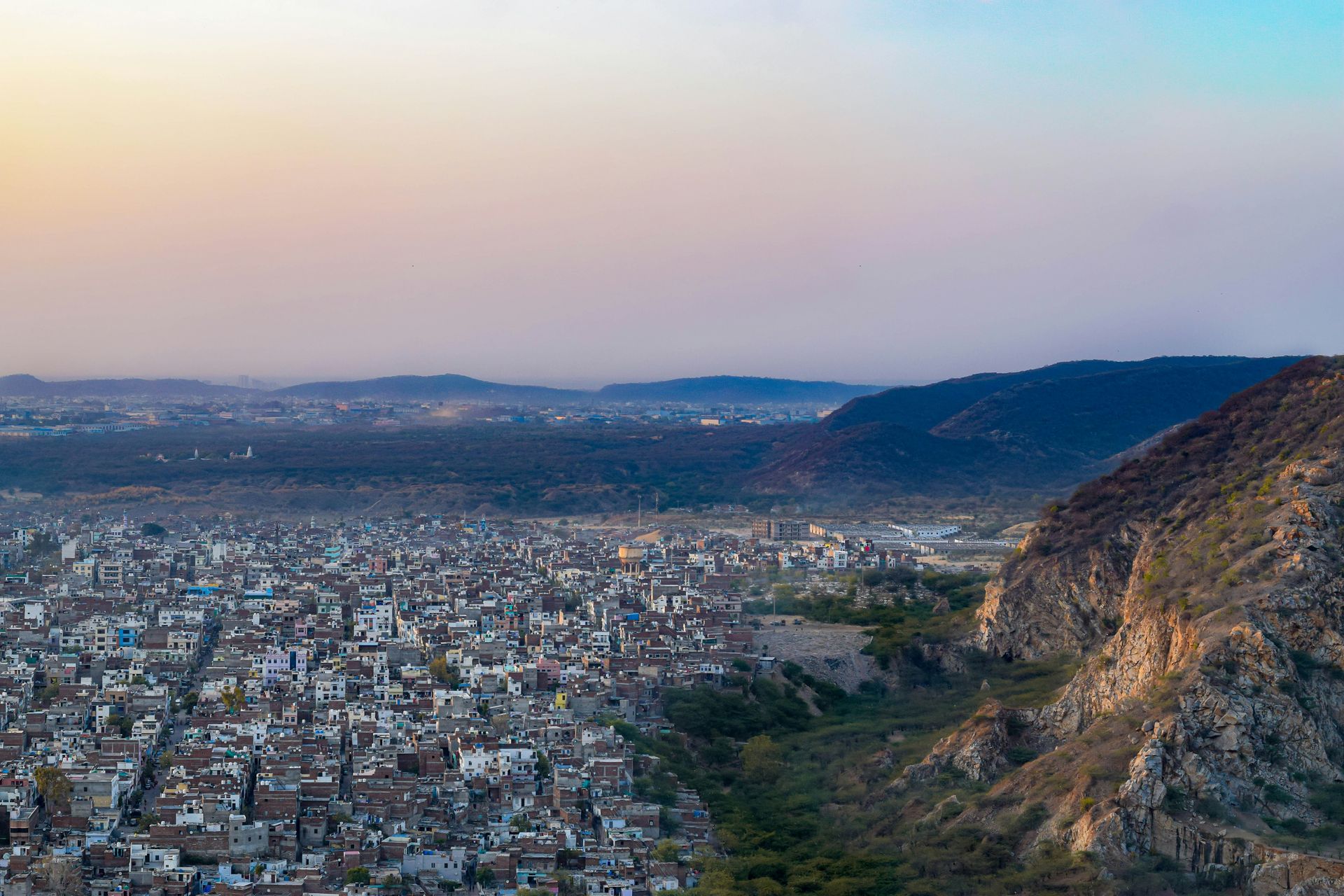 City nestled at the base of a mountain range. Buildings spread out with a view of a hazy sky in Jaipur, India.