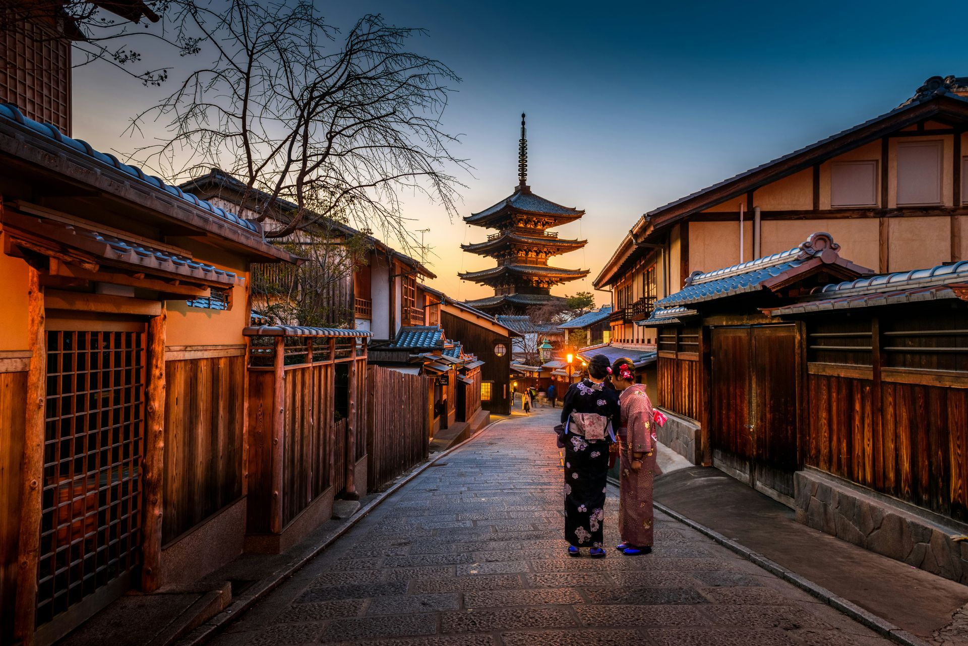 Stone street in Kyoto, Japan, with traditional buildings and pagoda. Two women in kimonos stand on the street. Dusk sky.