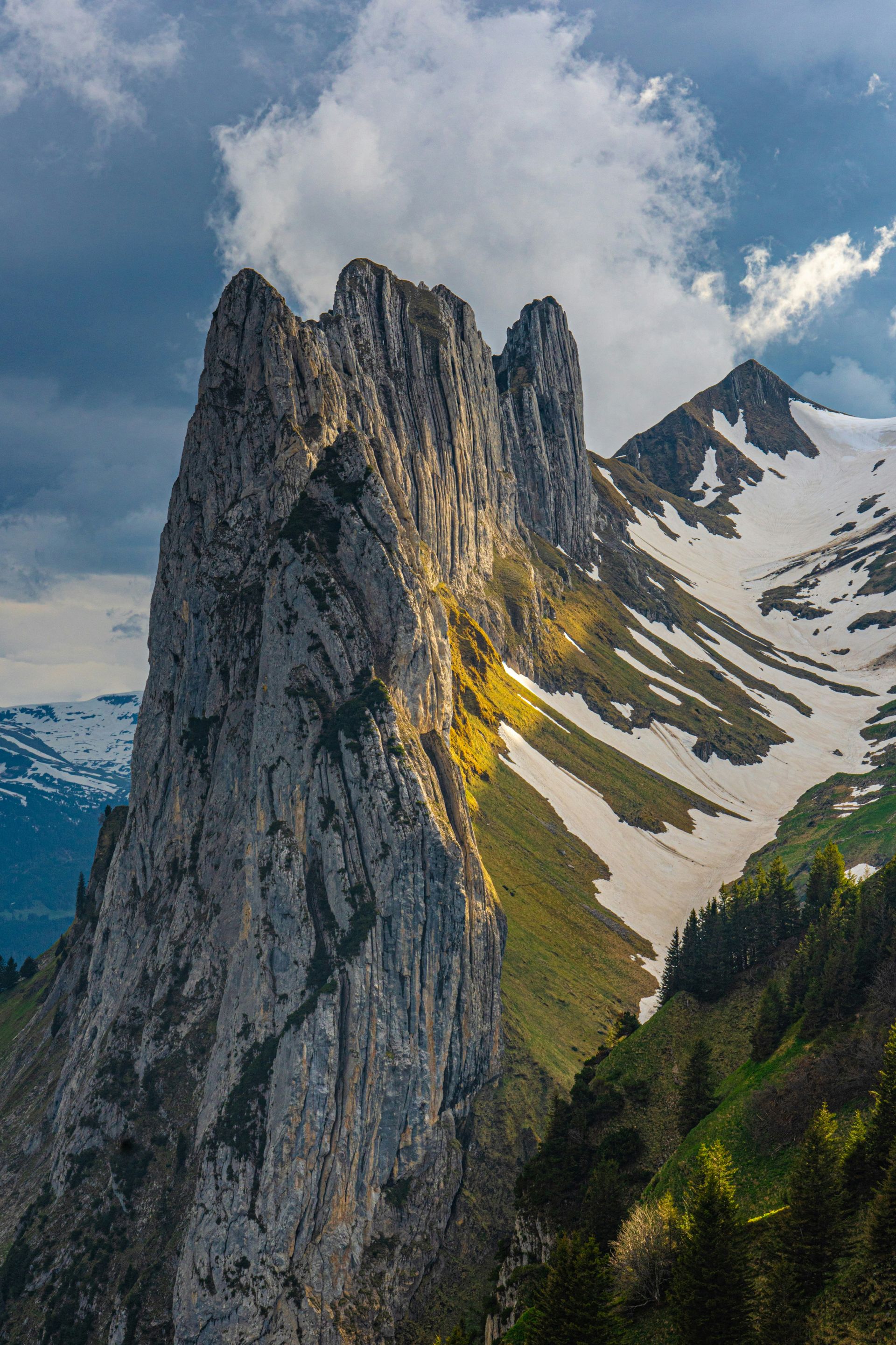 Jagged mountain peak with snow patches, illuminated by sunlight in Schwende, Switzerland.