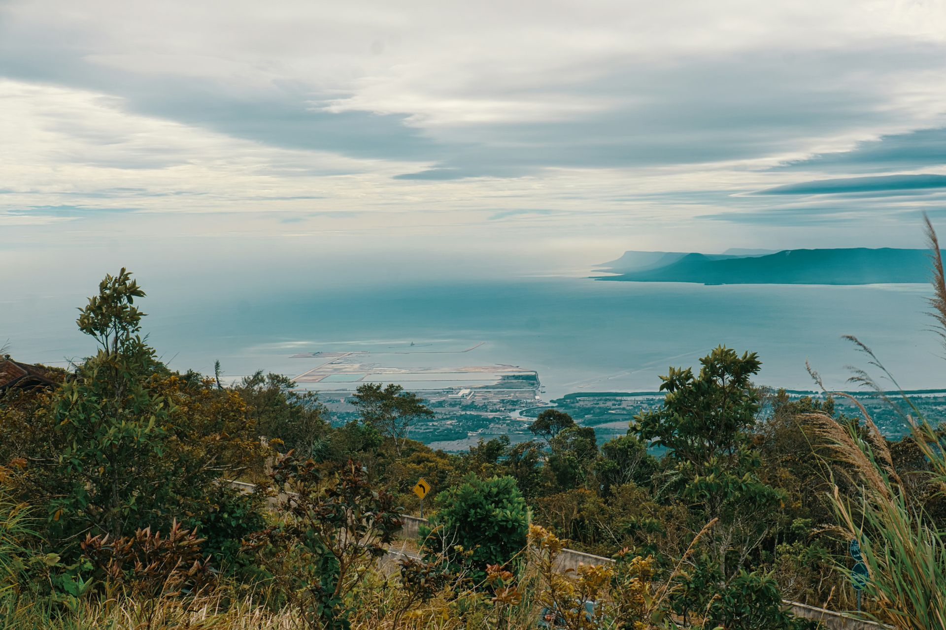 Overlooking blue ocean and land from a hilltop, green foliage in the foreground in Kampot, Cambodia.
