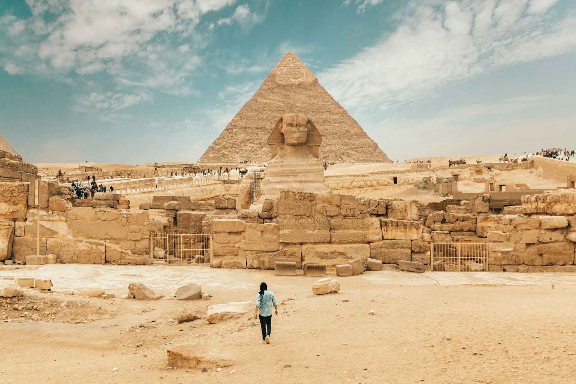 A man is walking in front of a pyramid and a sphinx in the desert in Cairo, Egypt.