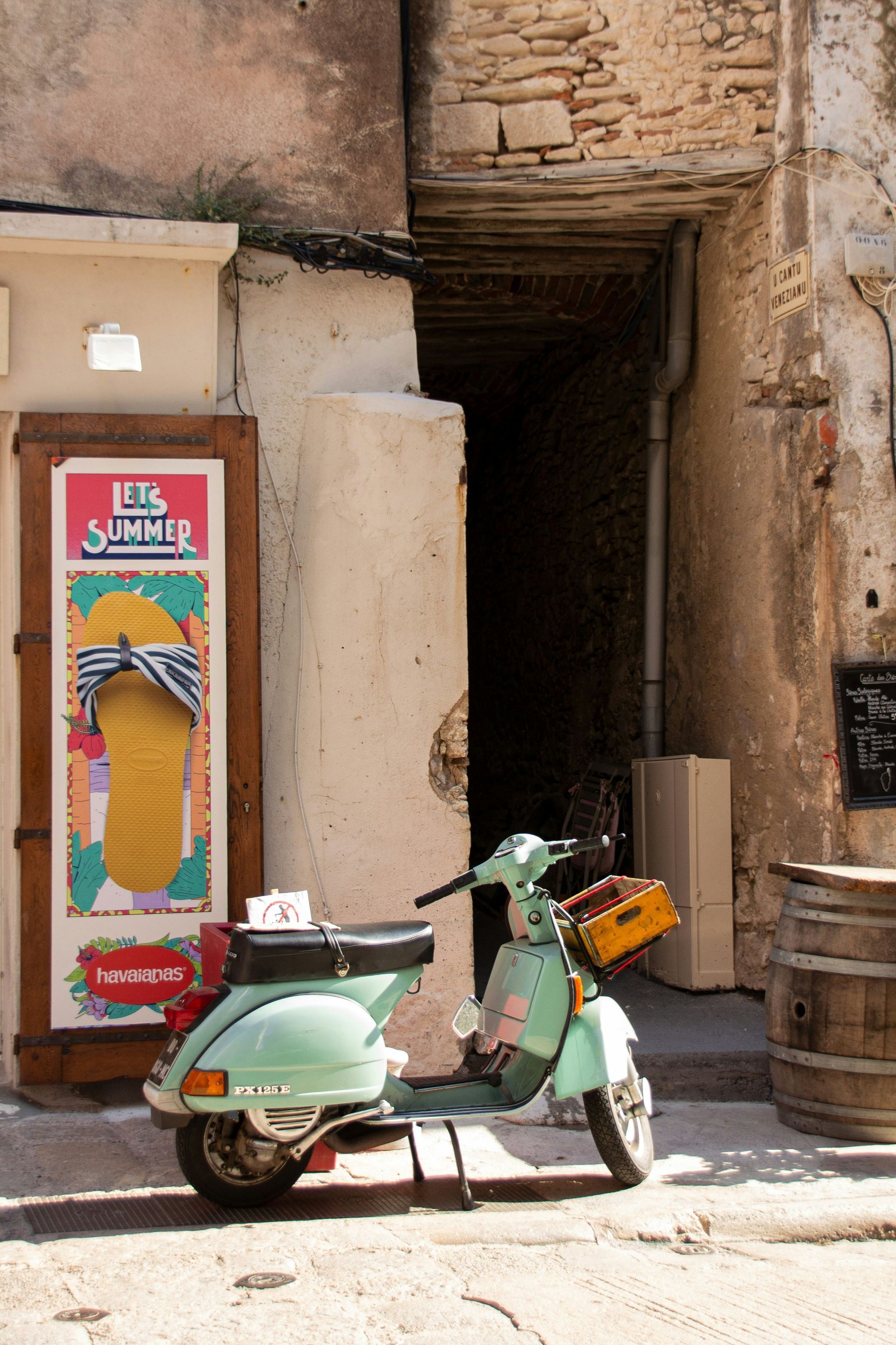 A green scooter is parked in front of a building in Corsica, France.