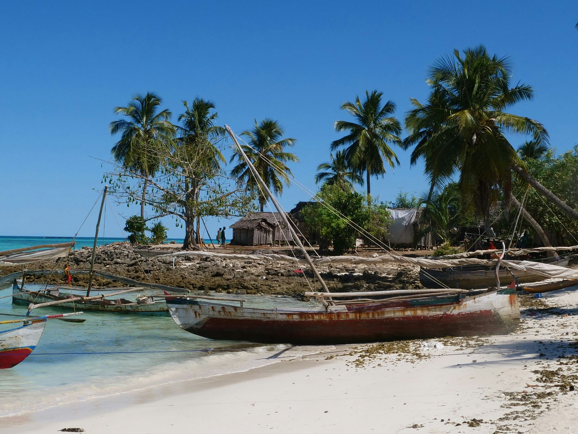 Tropical beach scene with weathered boats, palm trees, and small huts on Nosy Iranj, Madagascar.