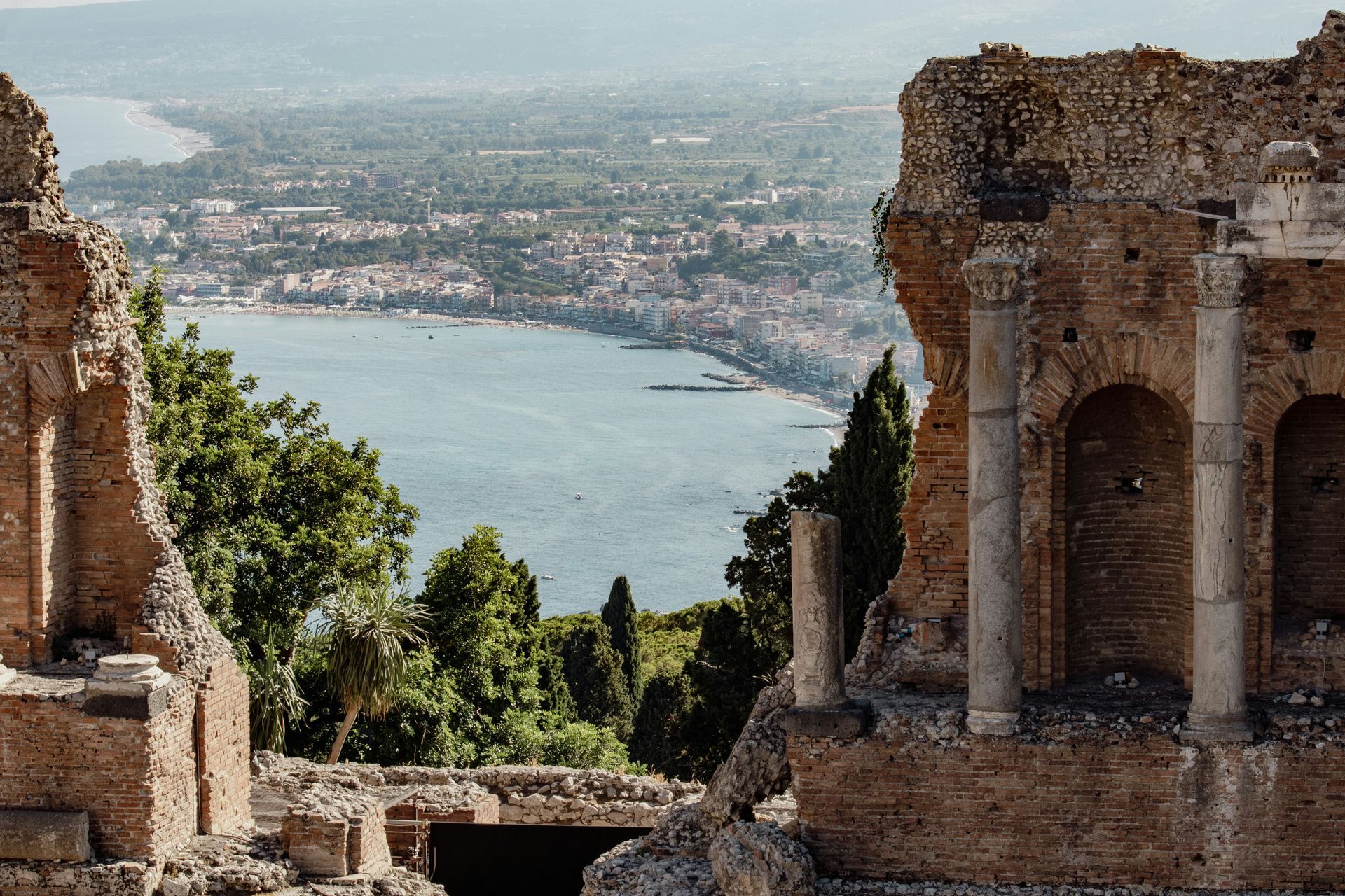 A small town sits on the shore of a large body of water in Sicily, Italy.