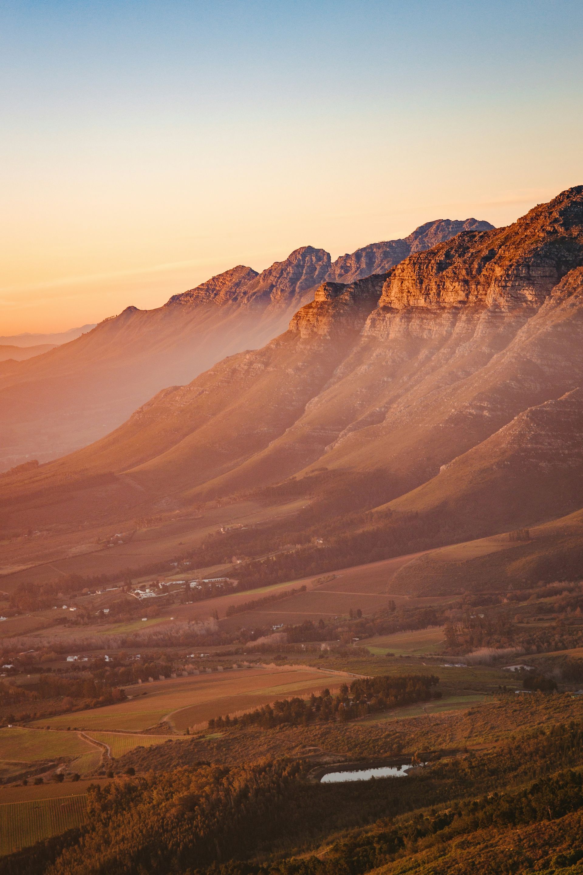 Golden light bathes a mountain range at sunset, casting long shadows over a valley in Stellenbosch, South Africa.