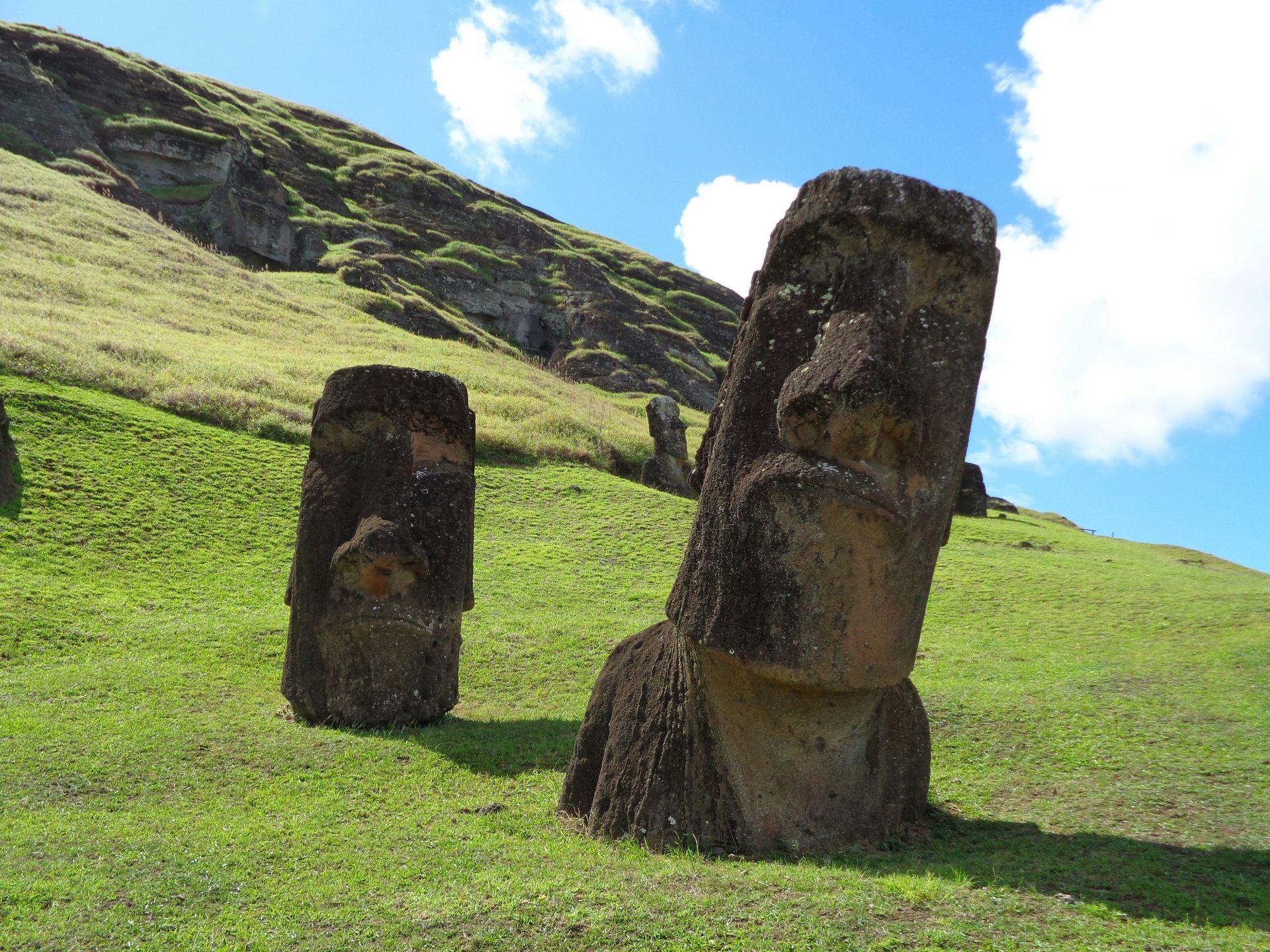 Two weathered Moai statues on a grassy hillside under a blue sky on Easter Island.