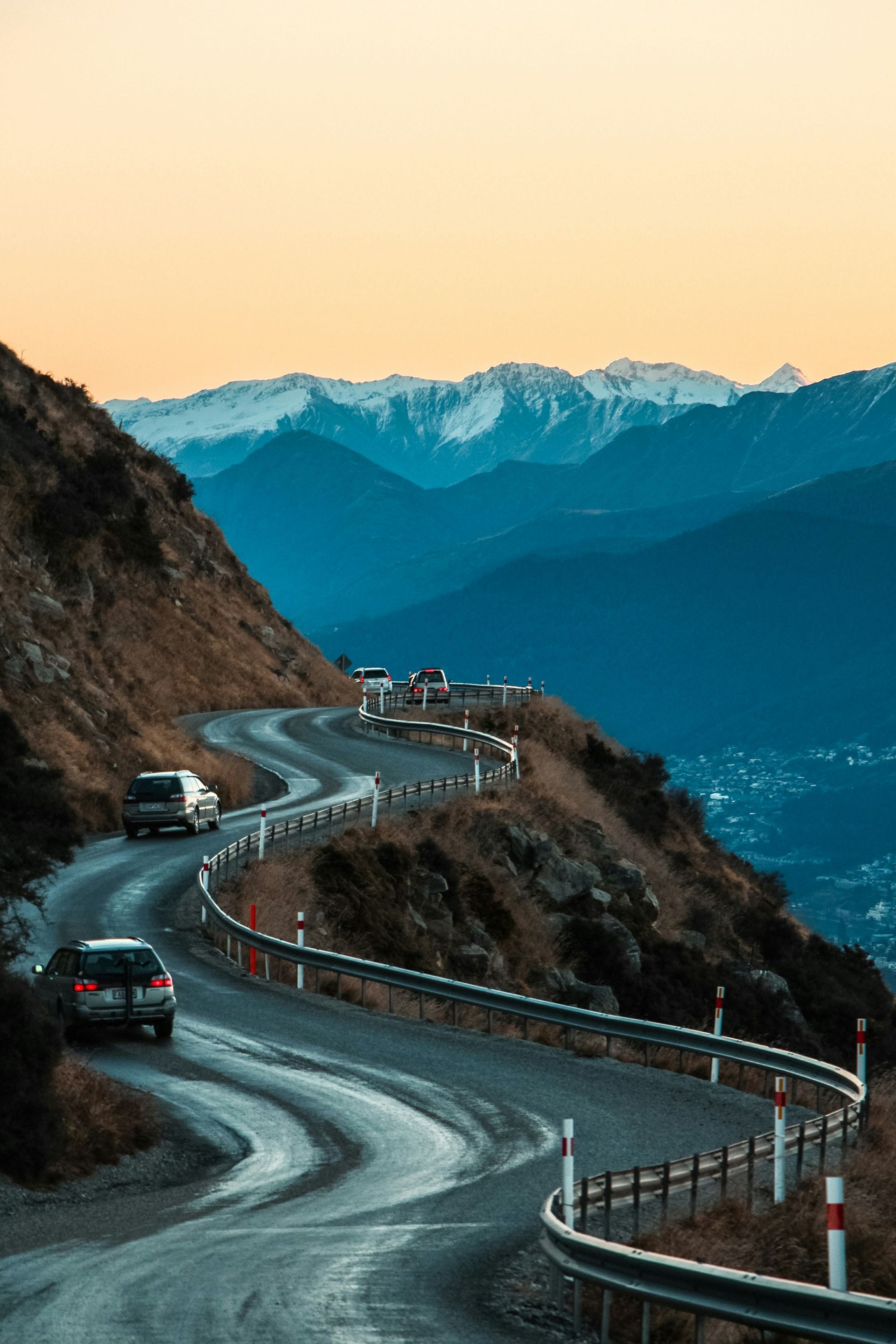 Cars are driving down a winding road in the mountains in Queenstown, New Zealand.