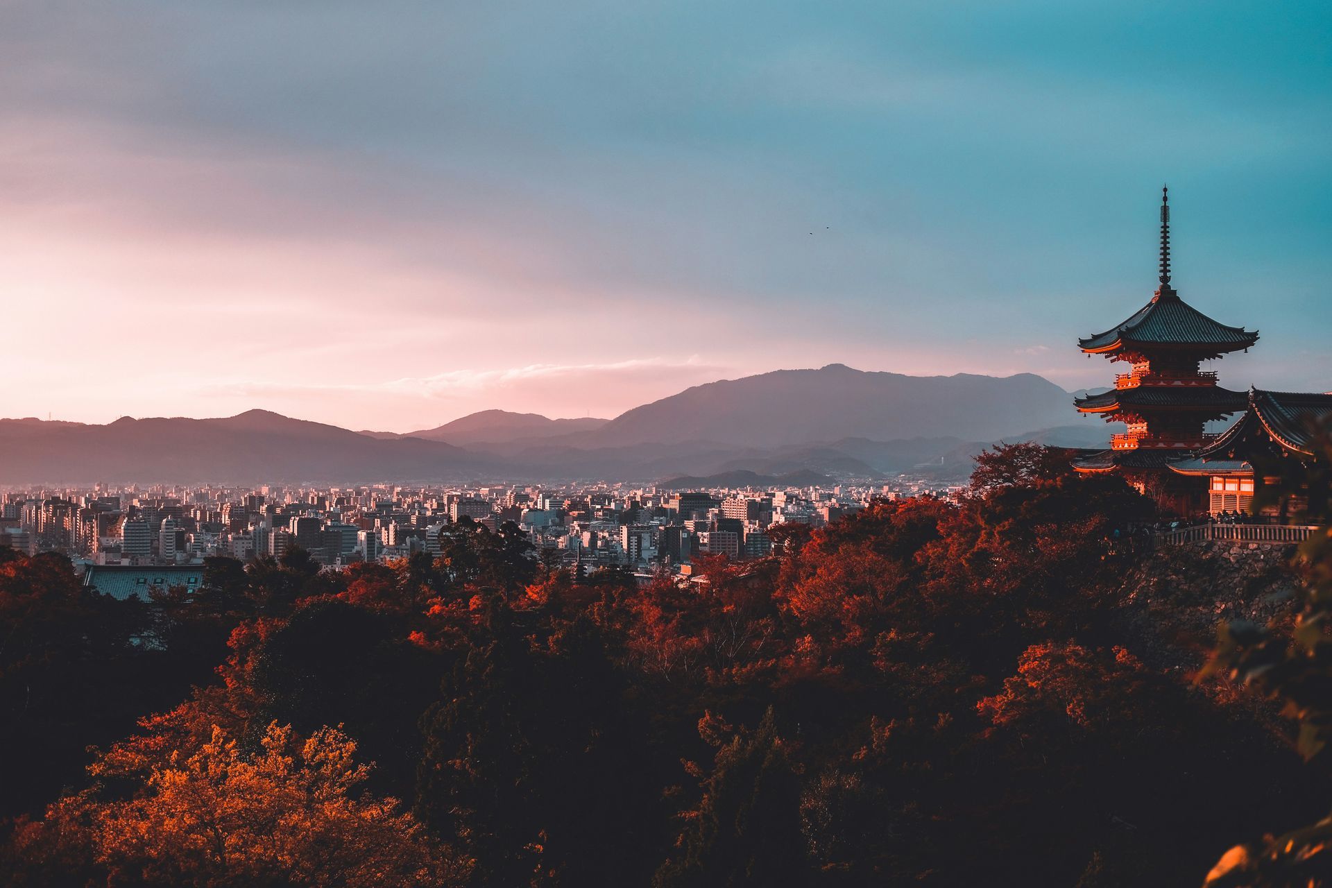 Kyoto, Japan at dusk, with pagoda in the foreground, cityscape, mountains, and colorful sky.