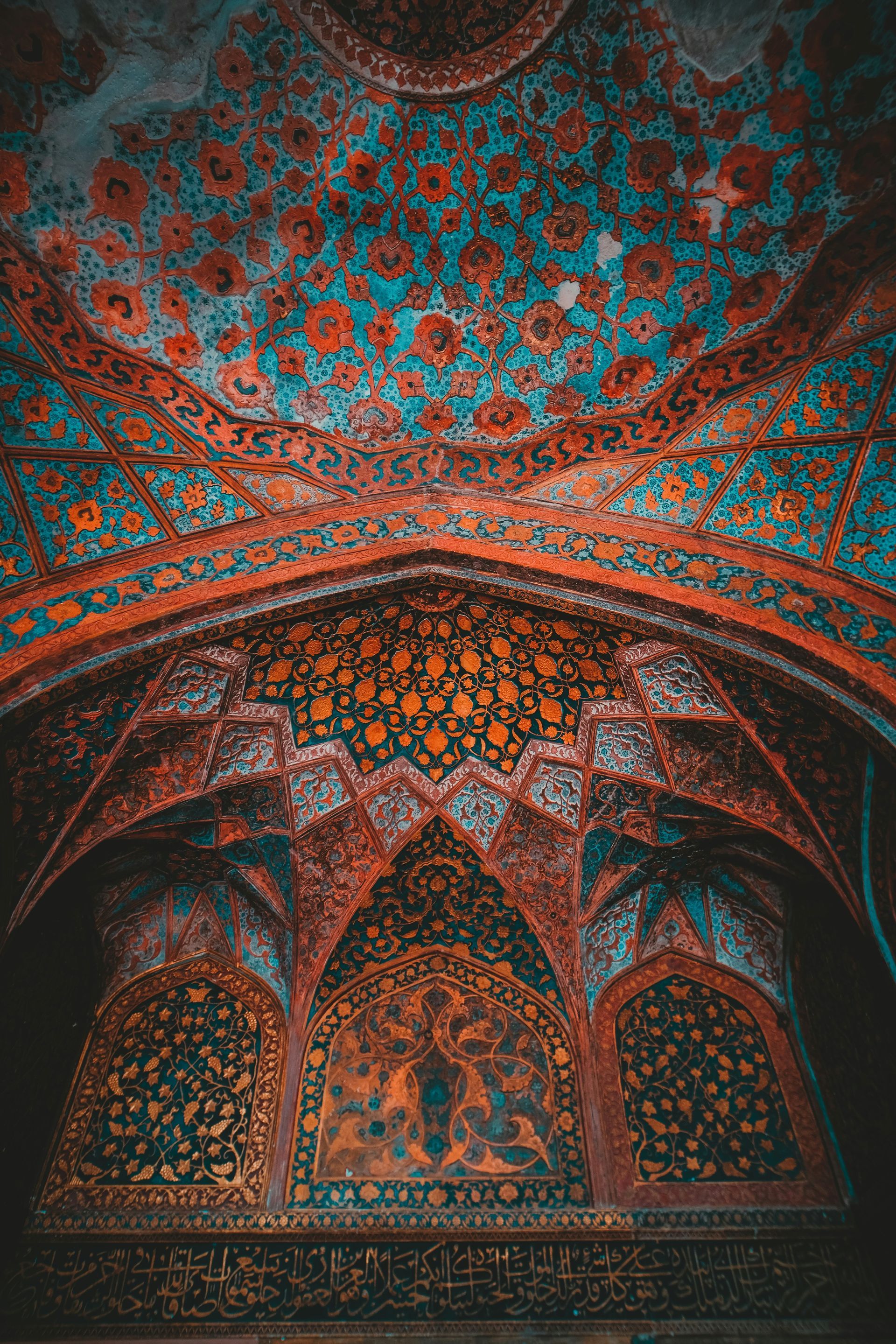Ornate, decorated ceiling with floral patterns in shades of blue, orange, and gold in Agra, India.