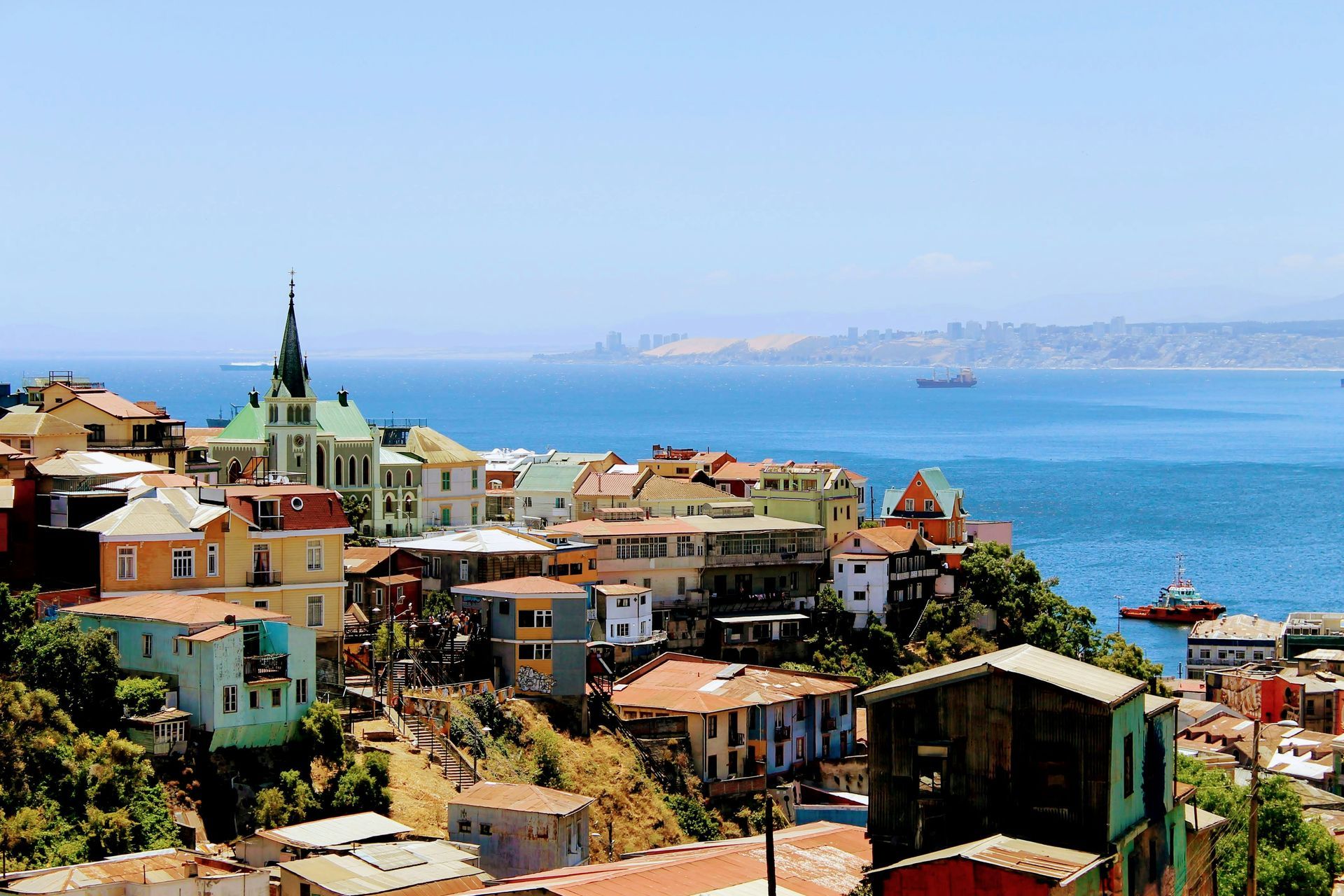 Colorful hillside houses overlooking the ocean in Valparaíso, Chile, under a clear blue sky.