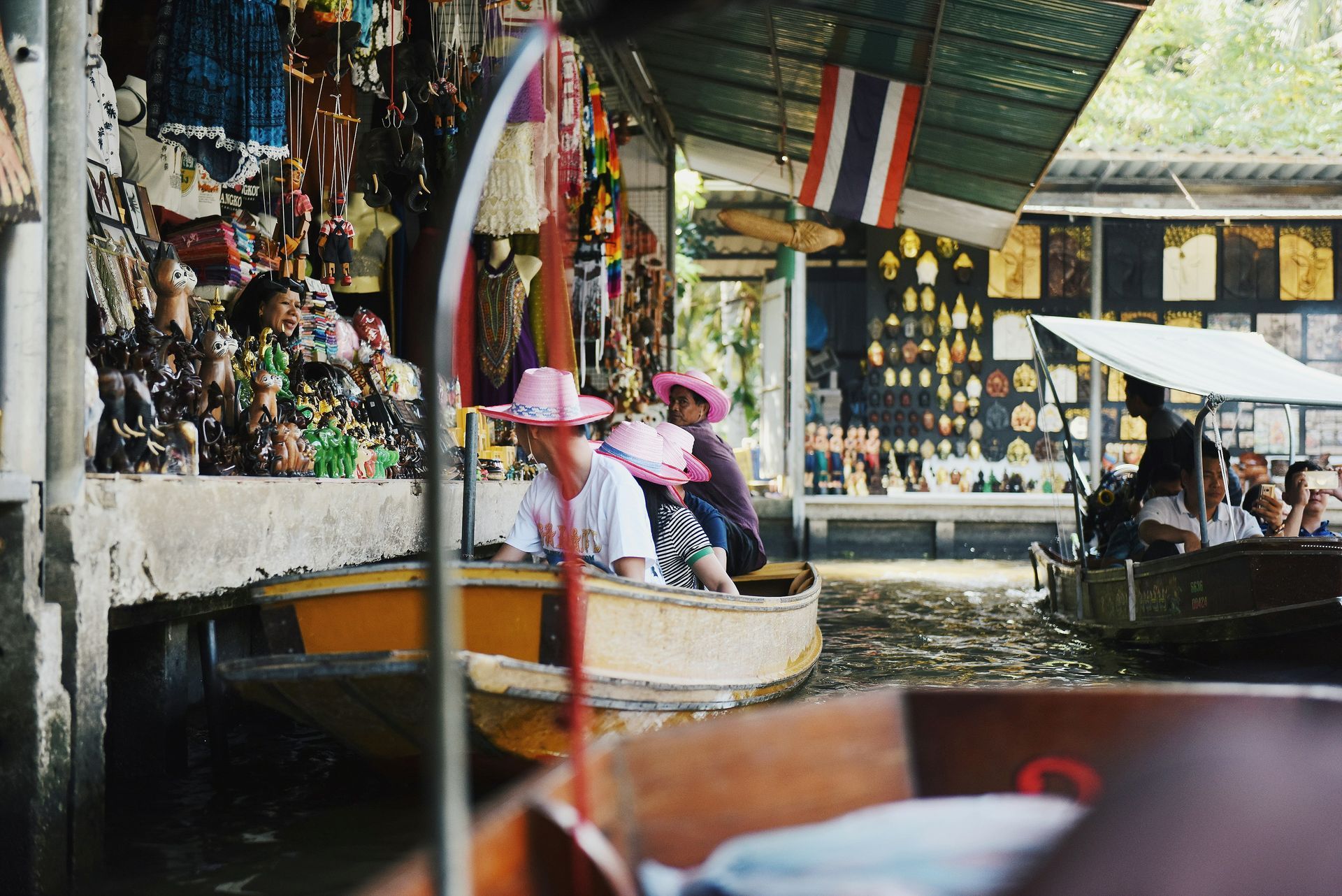 A woman in a pink hat is sitting in a boat on the Damnoen Saduak river market in Thailand.