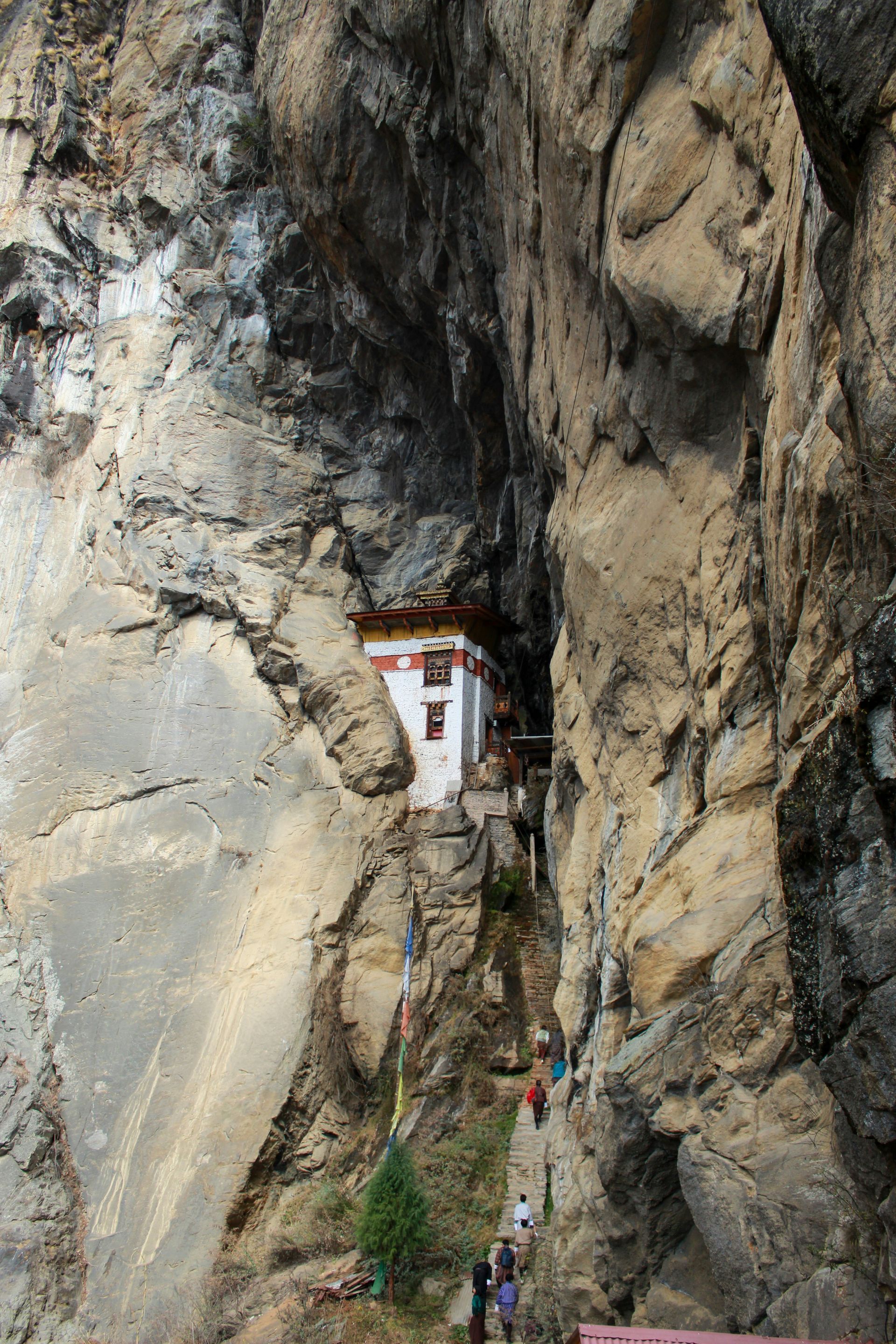 Paro Taktsang on a cliff, white and red, Bhutan; path with people ascends, surrounded by rock.
