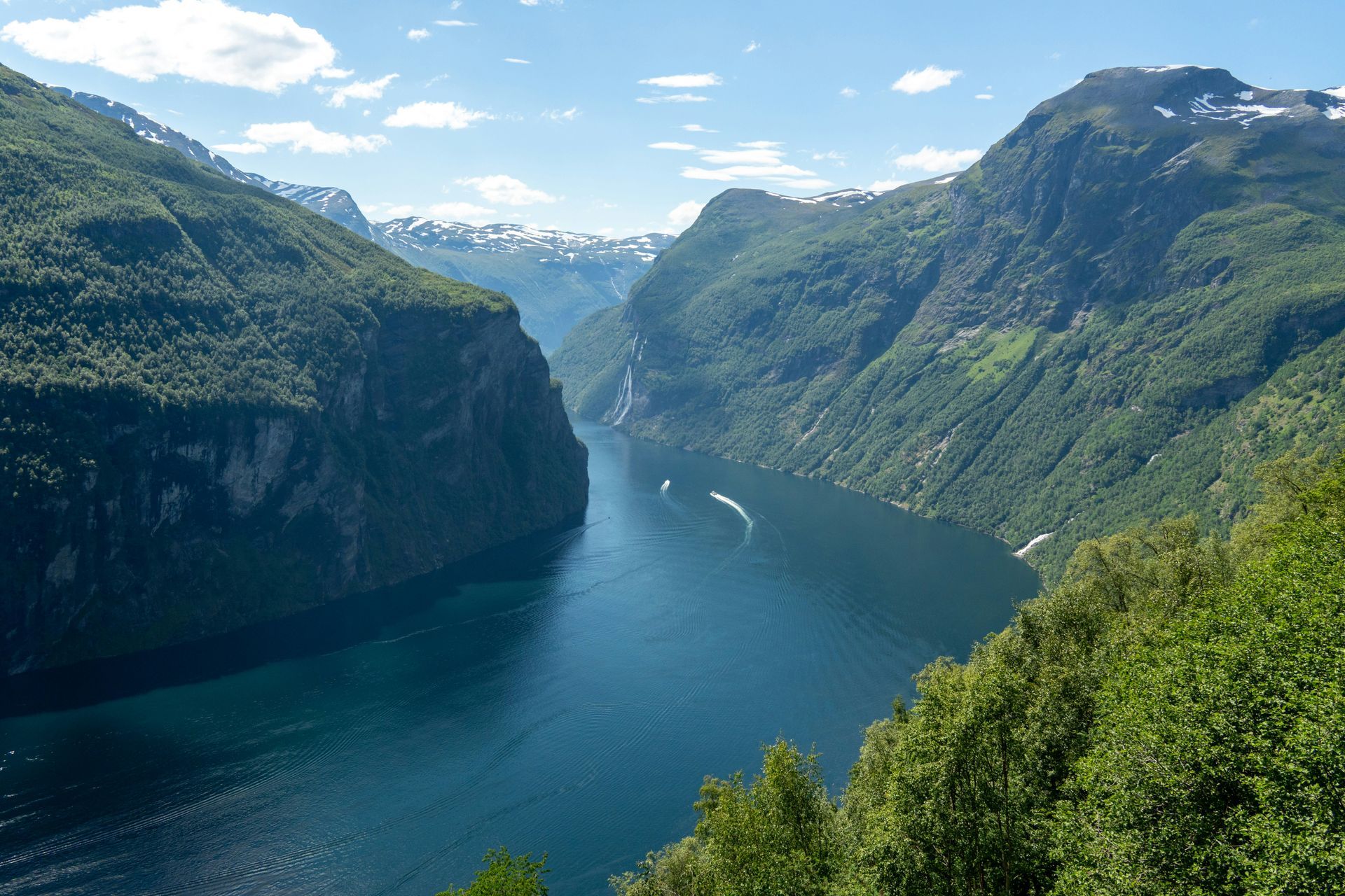 The Geirangerfjord with steep, green mountains on either side under a bright sky; boat in the water in Norway.
