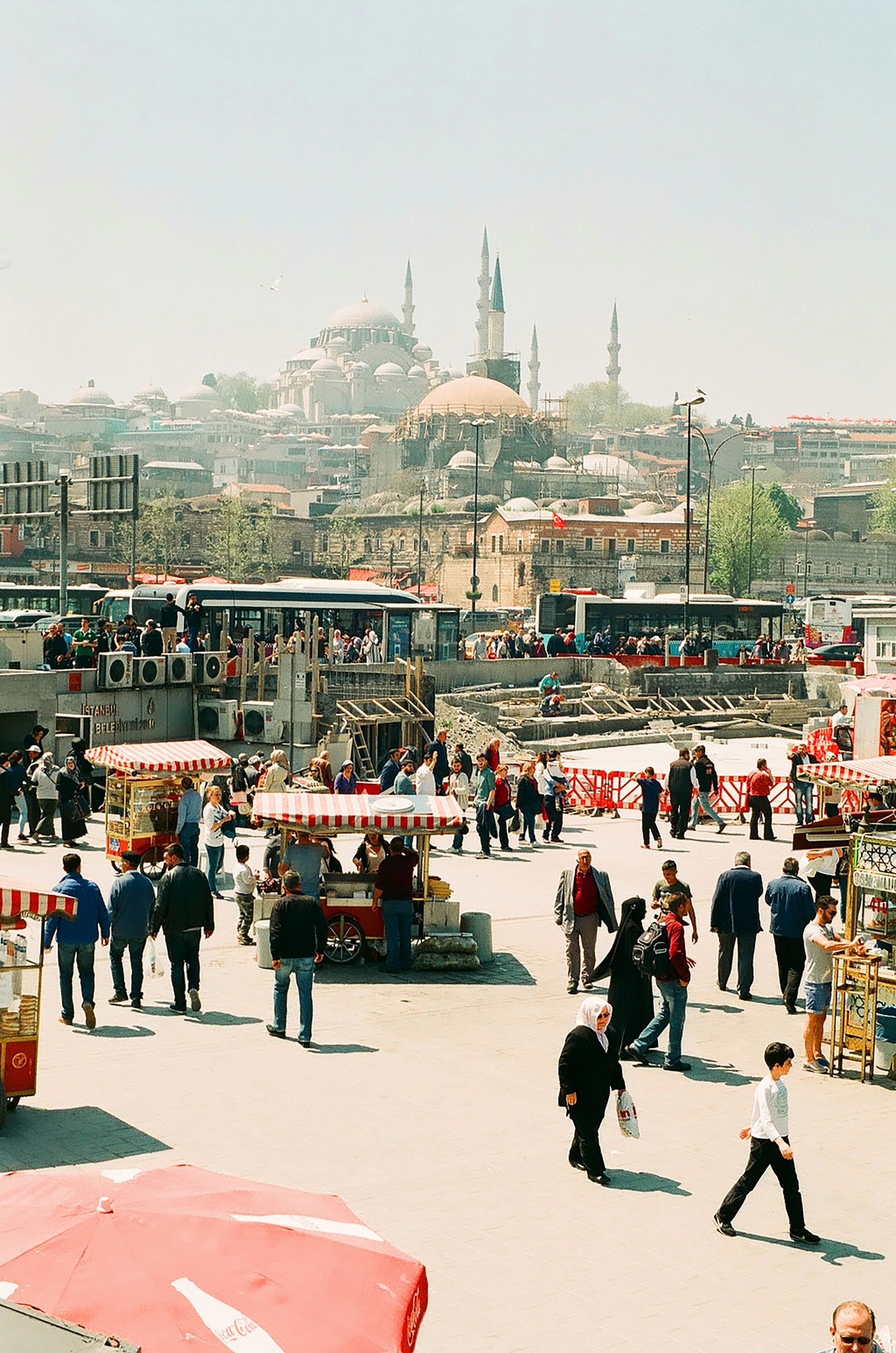 Busy Istanbul market square with vendors and people, historic buildings in background.