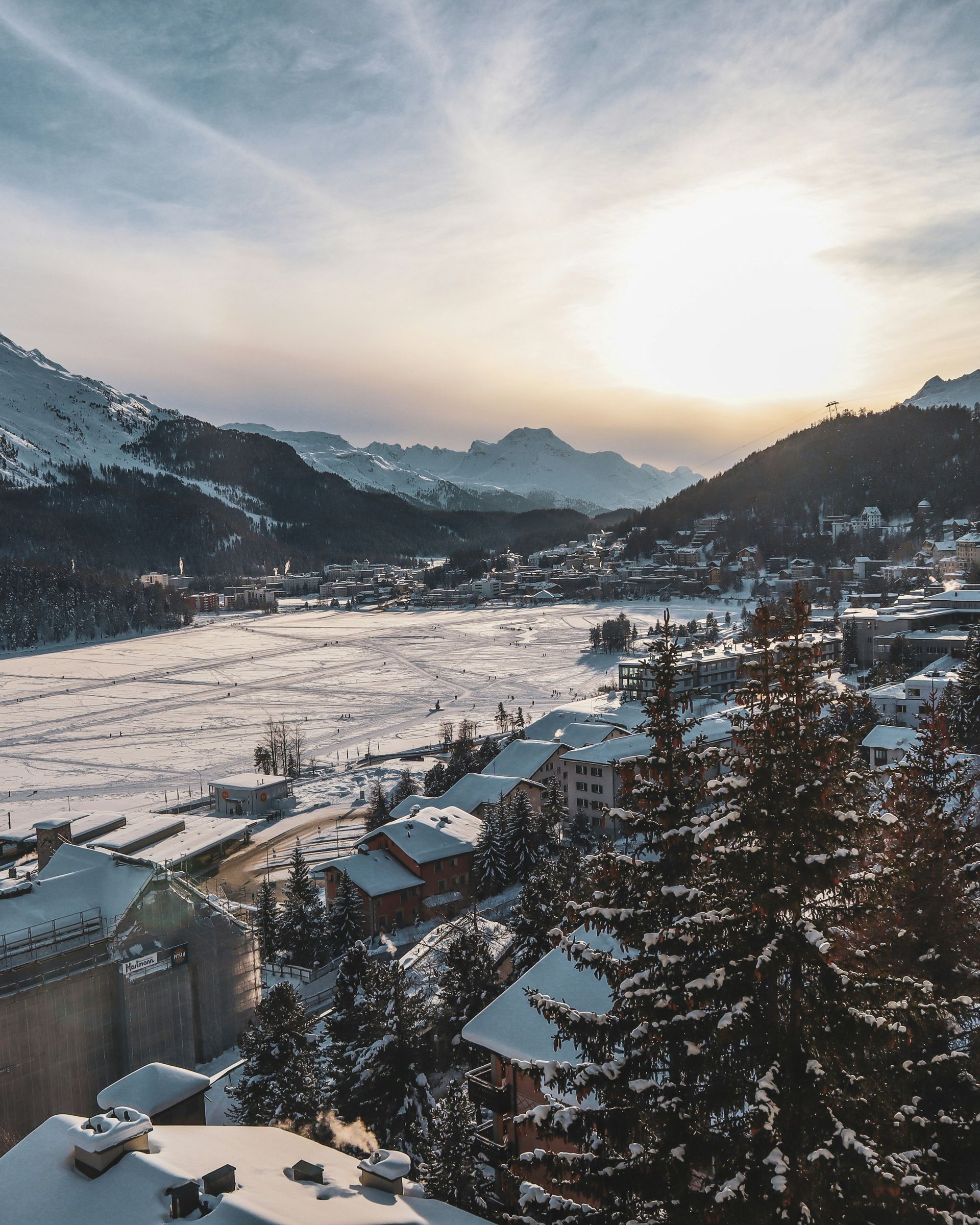 Snow-covered town of St. Moritz is nestled in a valley between mountains under a bright winter sky in Switzerland.