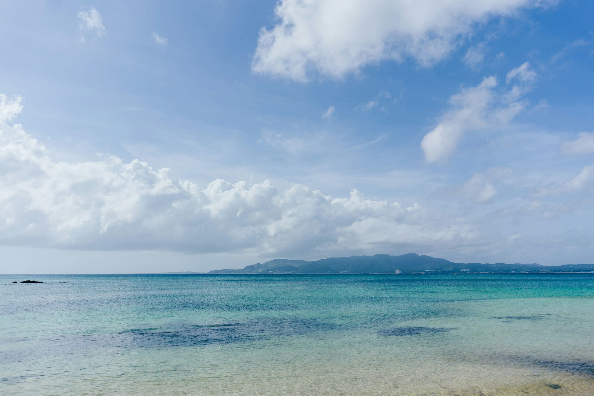 Azure ocean with a blue sky, white clouds, and a distant landmass in Okinawa, Japan.