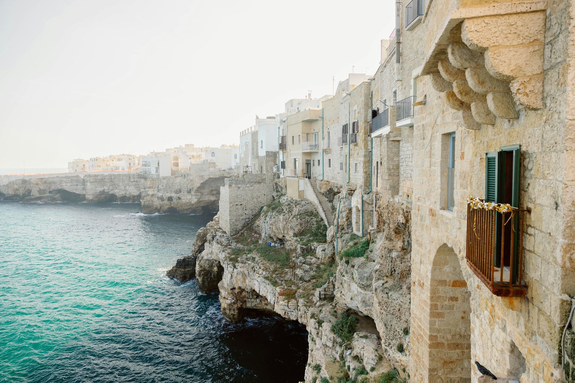 There is a balcony on the side of a building overlooking the ocean in Polignano a Mare, Italy.