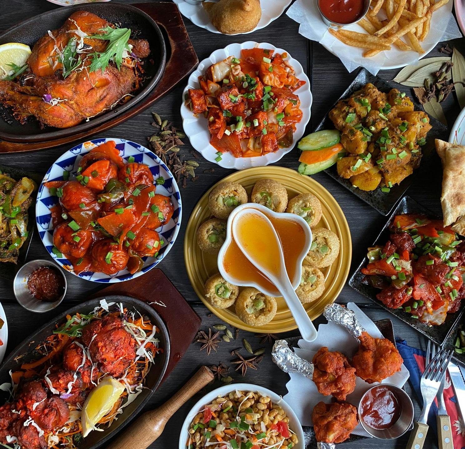 Assortment of Nepalese dishes, including chicken, curries, and pastries, arranged on a dark wooden table.