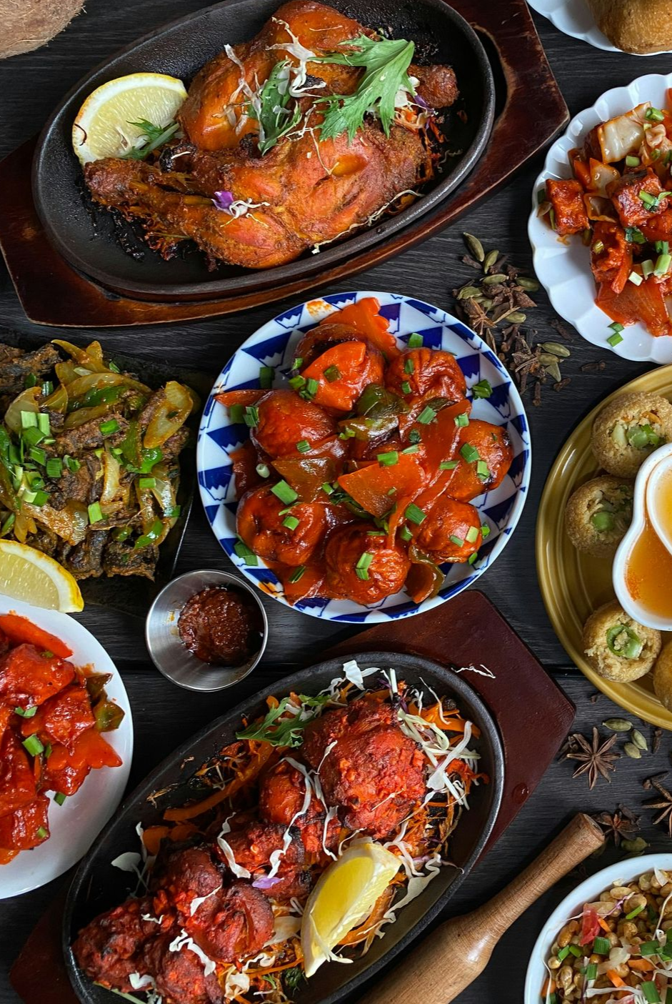 Assortment of Nepalese dishes, including chicken, curries, and pastries, arranged on a dark wooden table.