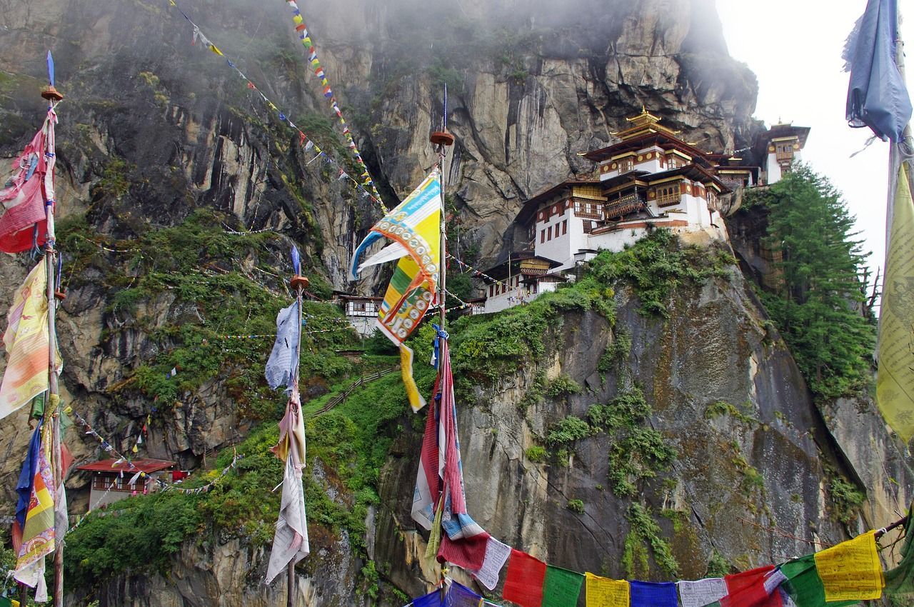 A group of flags are flying in front of The Tiger's Nest Monastery on top of a mountain in Bhutan.