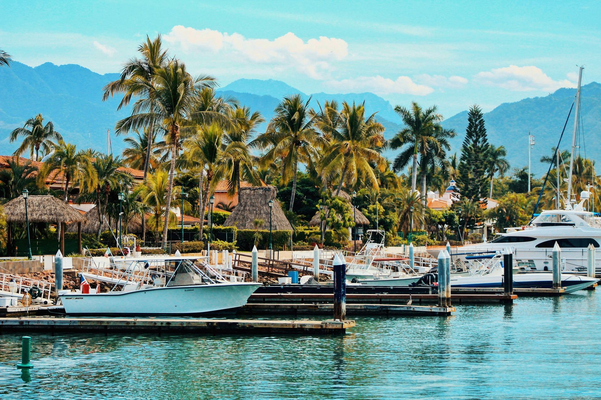 Boats docked in a marina with lush palm trees, buildings, and mountains in the background in Puerto Vallarta, Mexico.