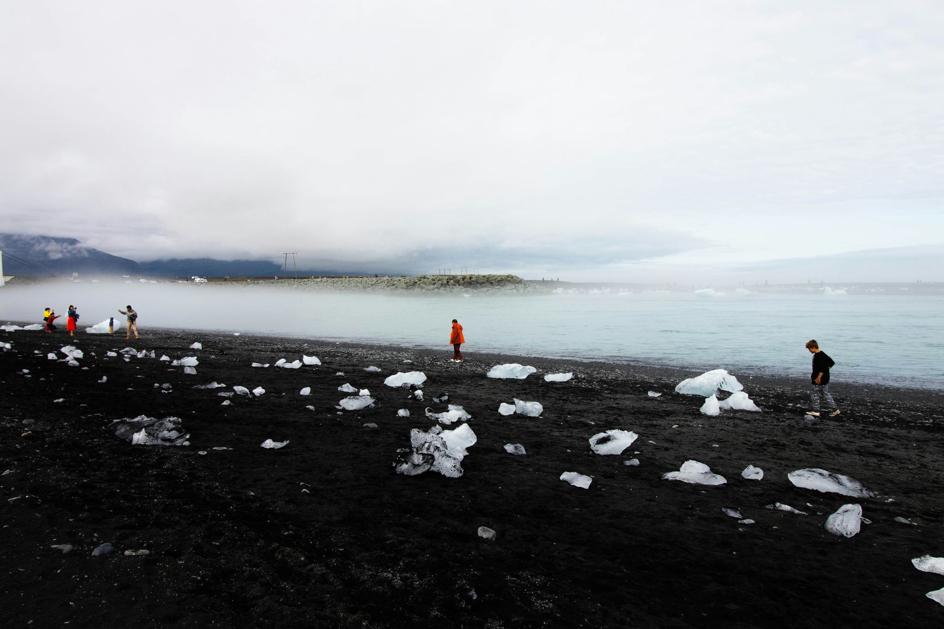 Black sand beach with ice chunks, people, and misty sea at Diamond Beach, Iceland.