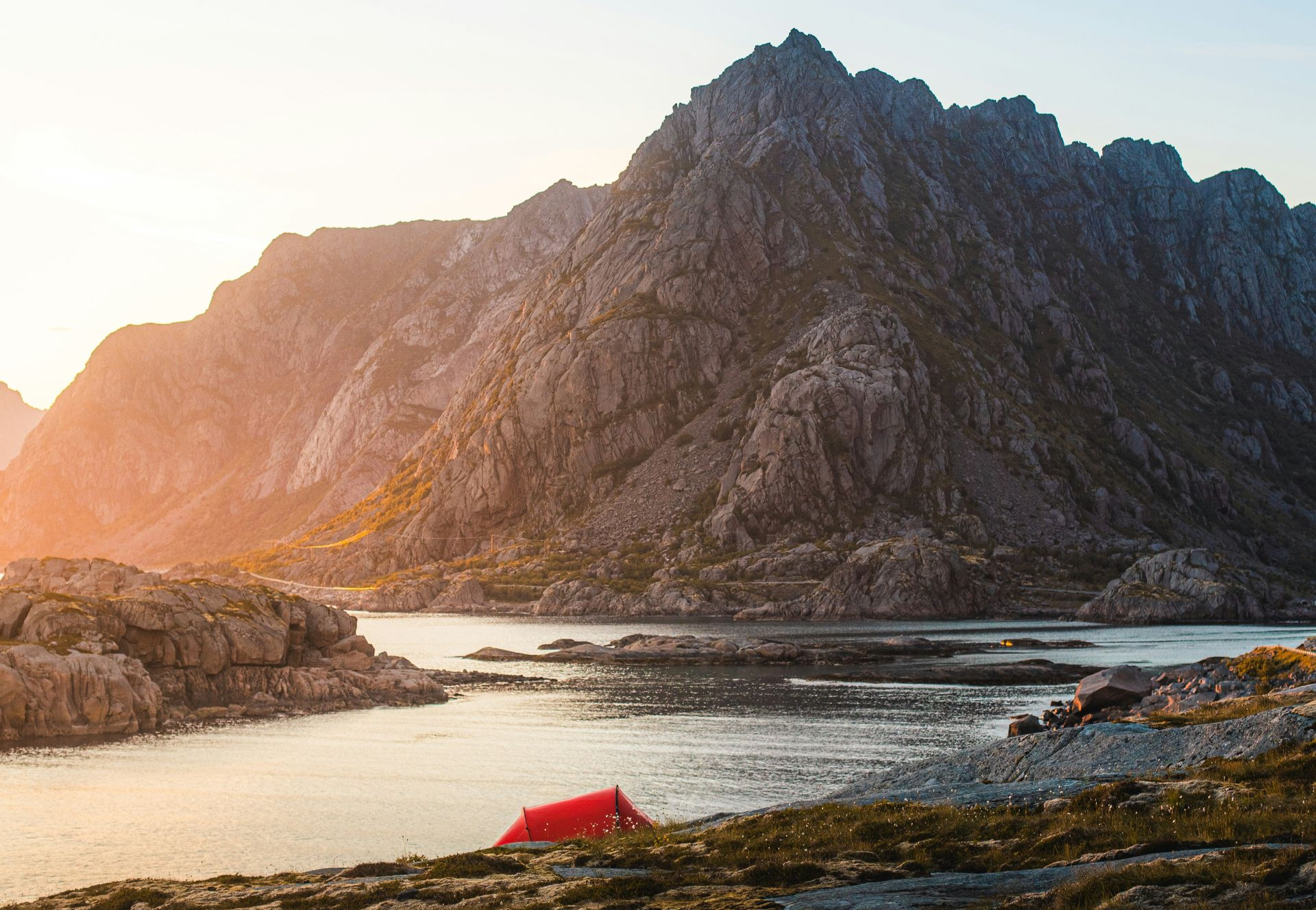 Red tent near a lake, overlooked by large mountains at sunset in Norway.
