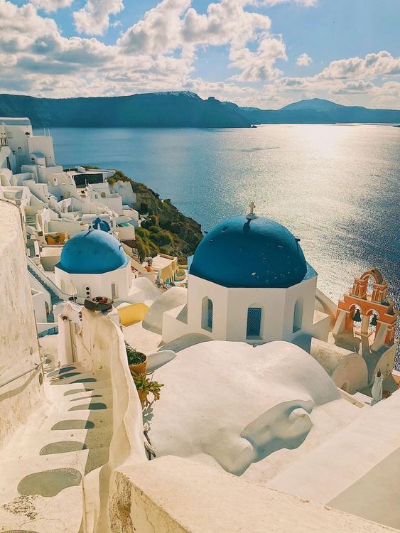 A row of white buildings with blue domes overlooking a body of water.