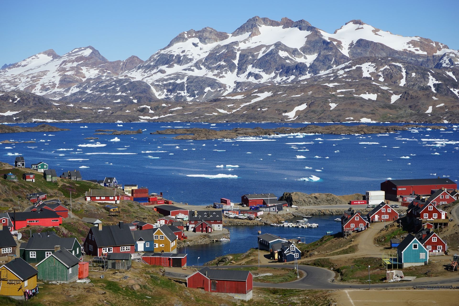 Colorful village of Tasiilaq by the ocean with snow-capped mountains in the background, in Greenland.