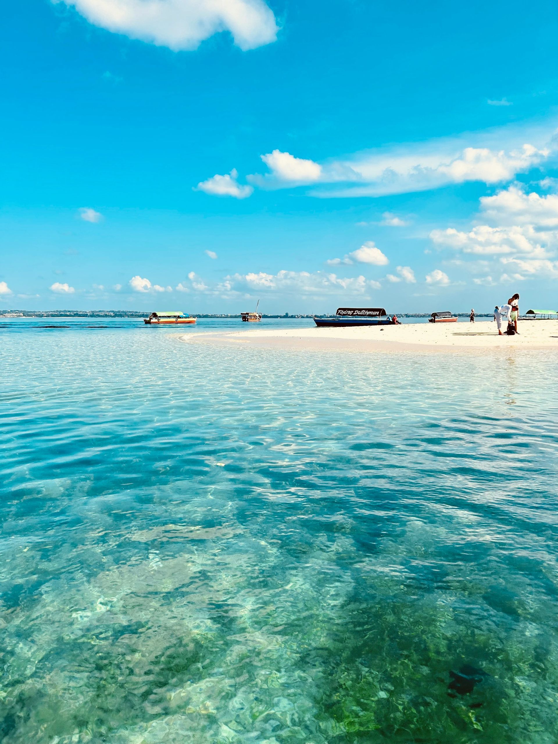 A person is standing on a sandy beach next to a body of water in Zanzibar, Tanzania.